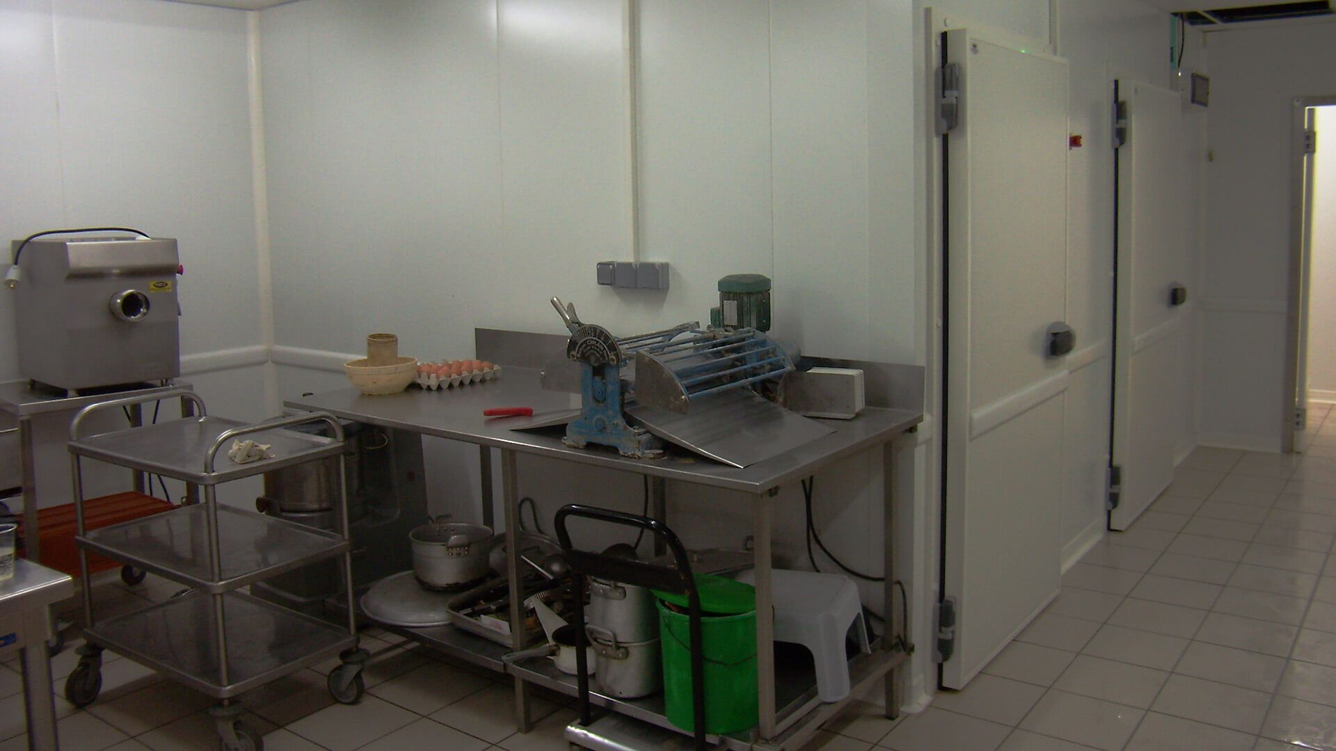 Cuisine équipée de tables et d'appareils en acier inoxydable, de portes de réfrigérateur et d'un espace de préparation des aliments.