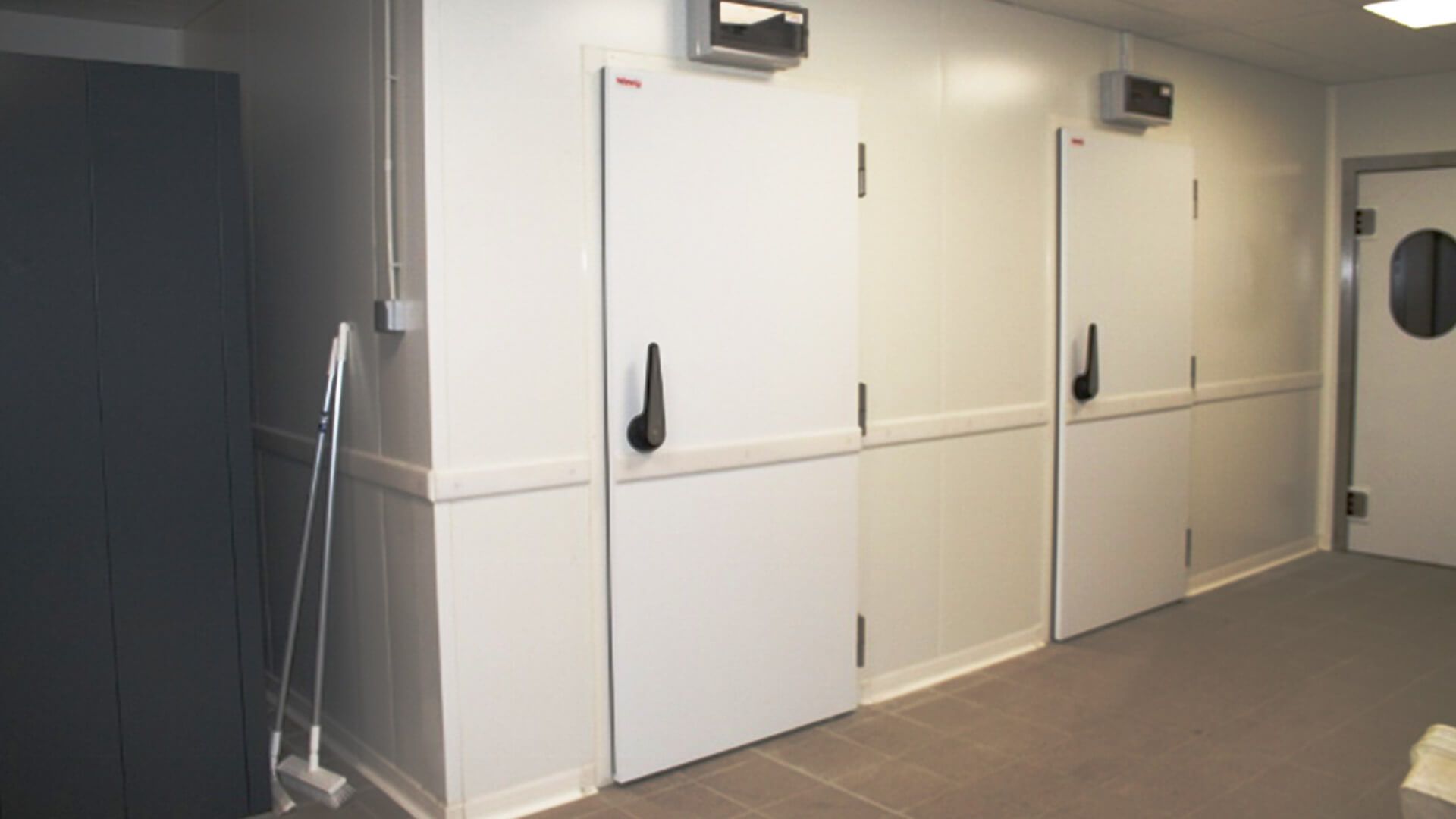 Portes industrielles blanches dans un couloir au sol carrelé gris.