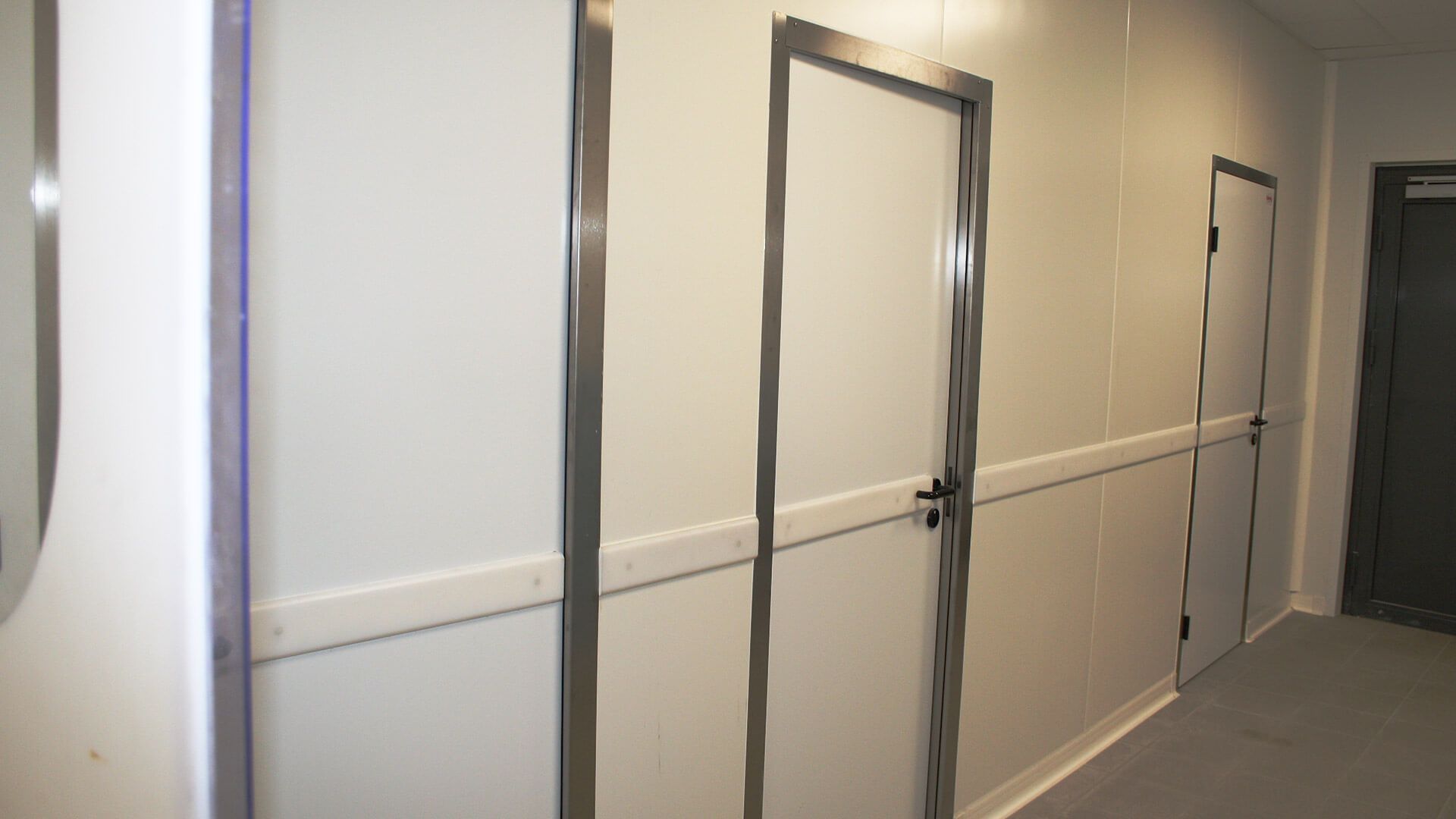 Couloir aux murs, portes et rampe blancs. Encadrements de portes argentés.