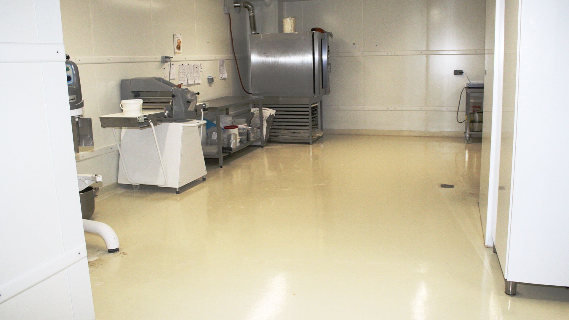 Intérieur d'une cuisine professionnelle avec des équipements en acier inoxydable et un sol jaune pâle.