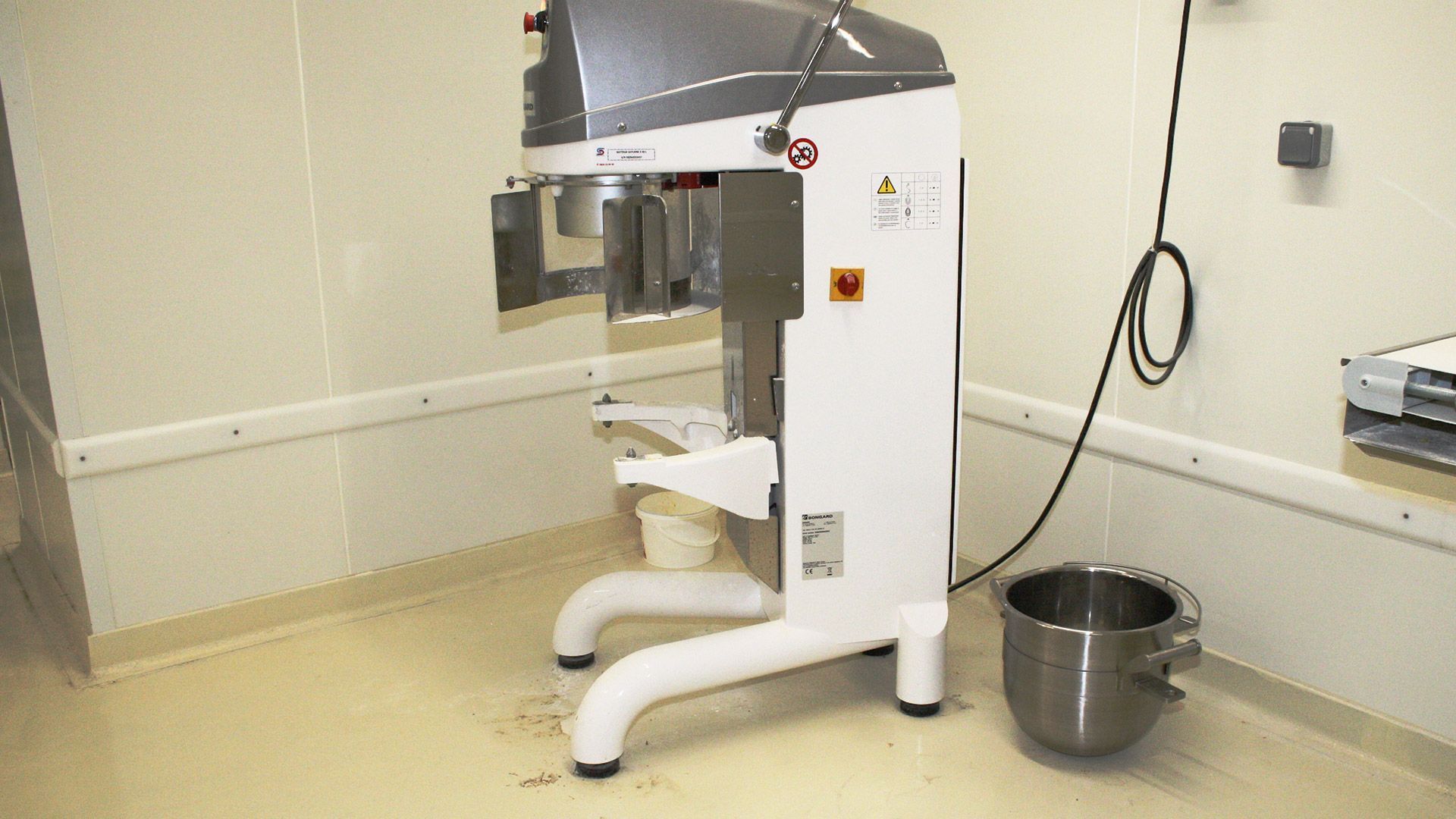 Mélangeur industriel blanc dans une pièce propre aux murs blancs, avec une cuve de mélange en acier inoxydable.