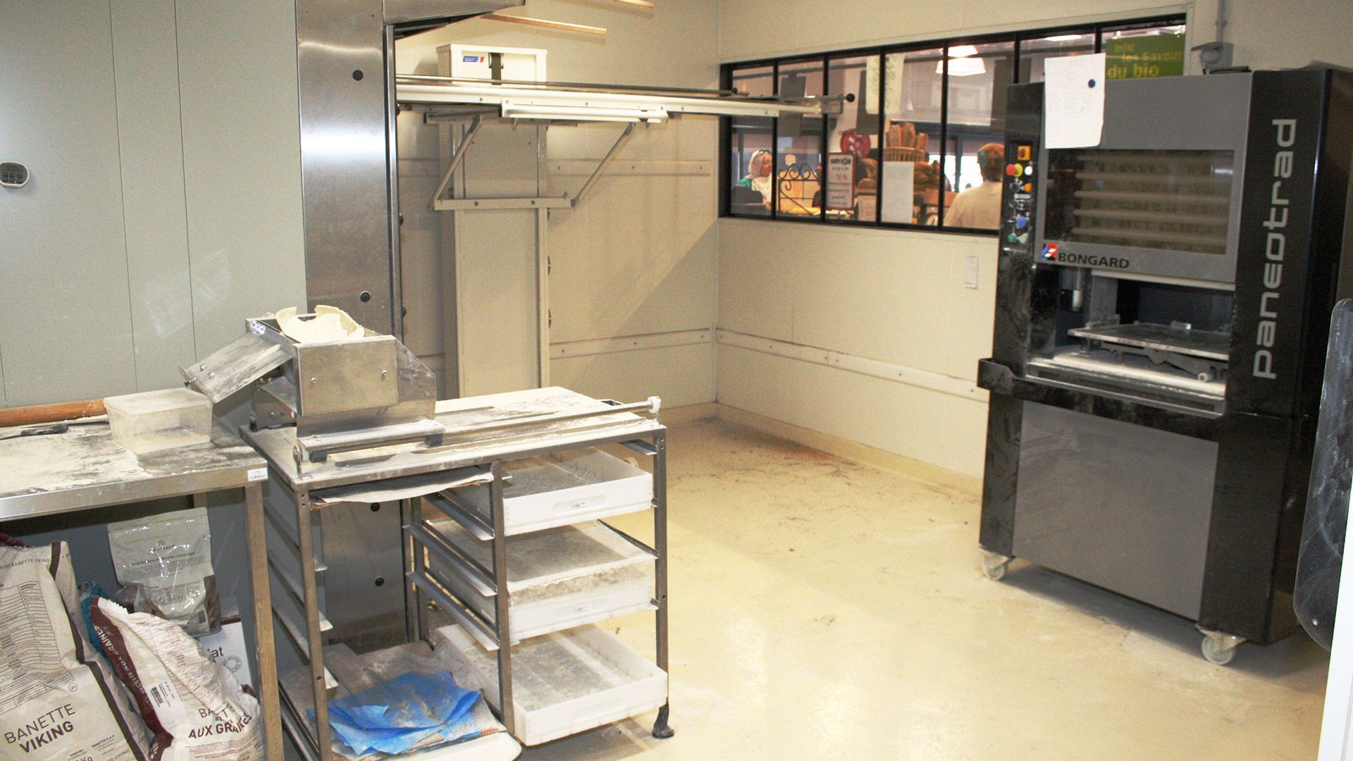 Cuisine de boulangerie vide avec four industriel, étagères métalliques et plans de travail.