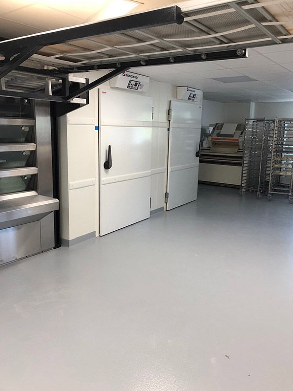 Cuisine professionnelle équipée de deux réfrigérateurs blancs et d'une étagère en acier inoxydable.