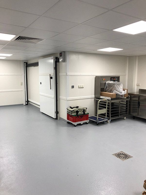 Une cuisine professionnelle équipée d'une chambre froide, d'appareils électroménagers en acier inoxydable et d'un sol gris.