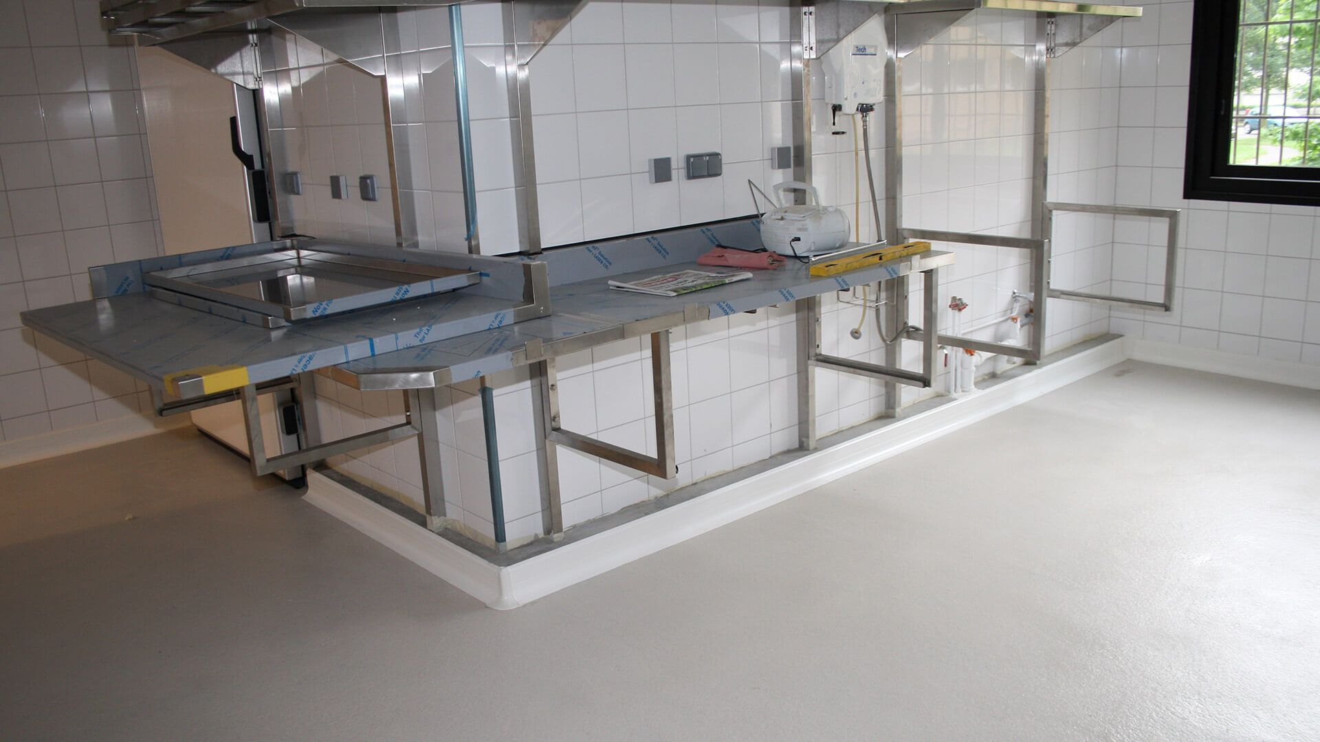 Zone de préparation des aliments en acier inoxydable dans une cuisine commerciale avec murs carrelés blancs et fenêtre.