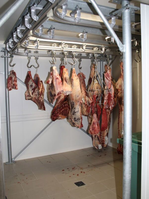 Carcasses de viande suspendues à des crochets dans une chambre froide.