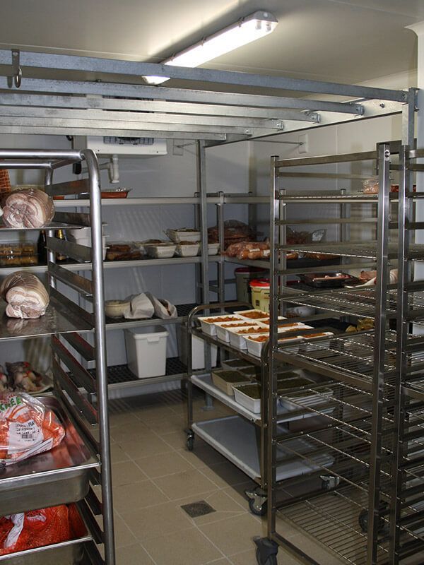 Chambre froide de cuisine commerciale avec étagères métalliques pour le stockage des aliments et des récipients.