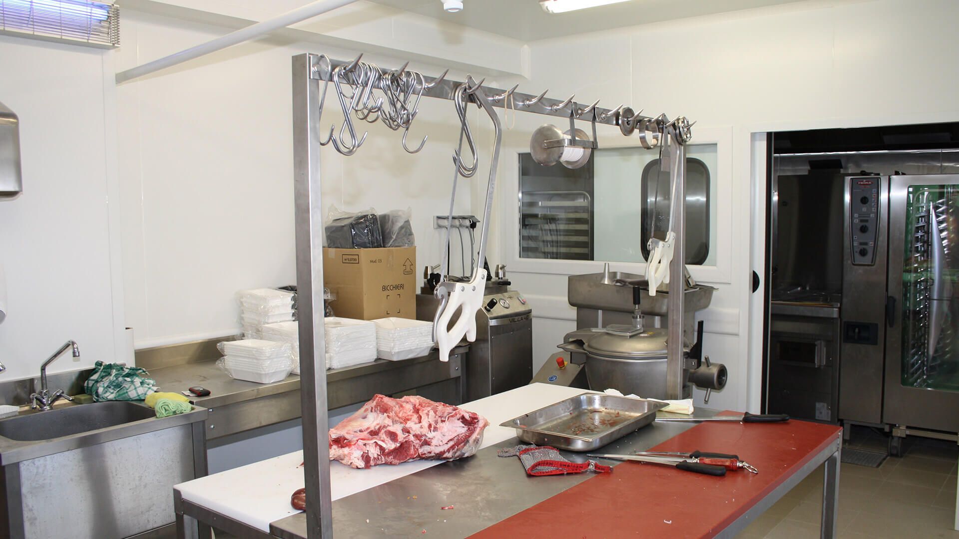 Intérieur d'une boucherie avec de la viande sur une table, des crochets au-dessus des têtes et du matériel industriel.