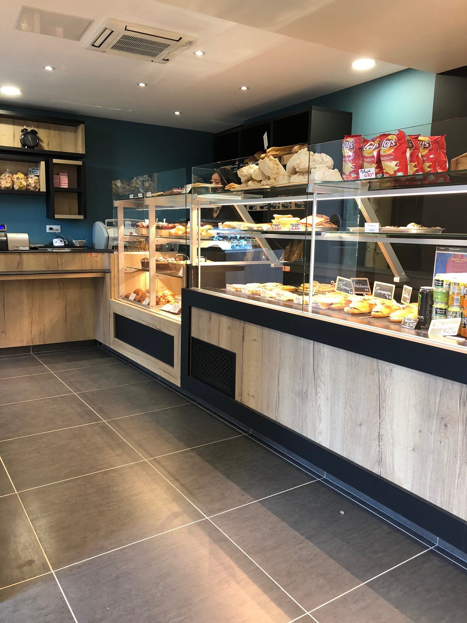 Intérieur d'une boulangerie avec vitrines remplies de pâtisseries, sol carrelé noir, mur d'accent bleu.