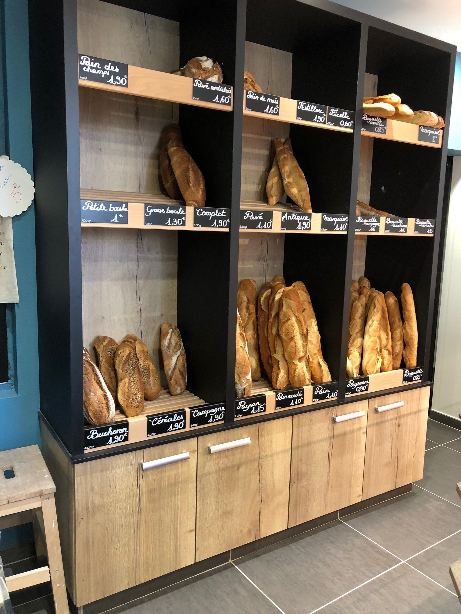 Vitrine de boulangerie avec différents types de pains sur des étagères, armoire en bois à cadre noir, étiquettes.