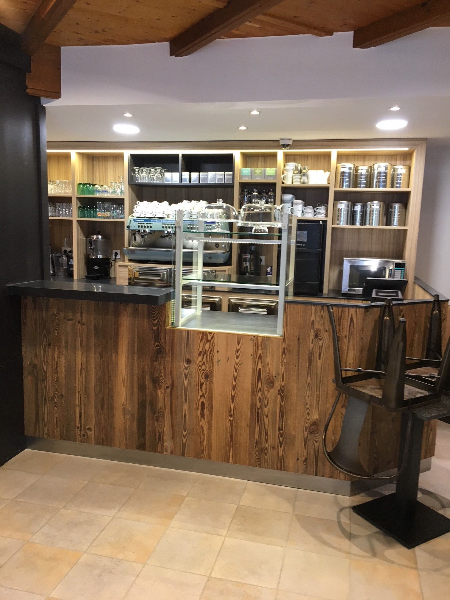 Un comptoir de café avec des panneaux de bois, des étagères remplies de fournitures et une petite vitrine.