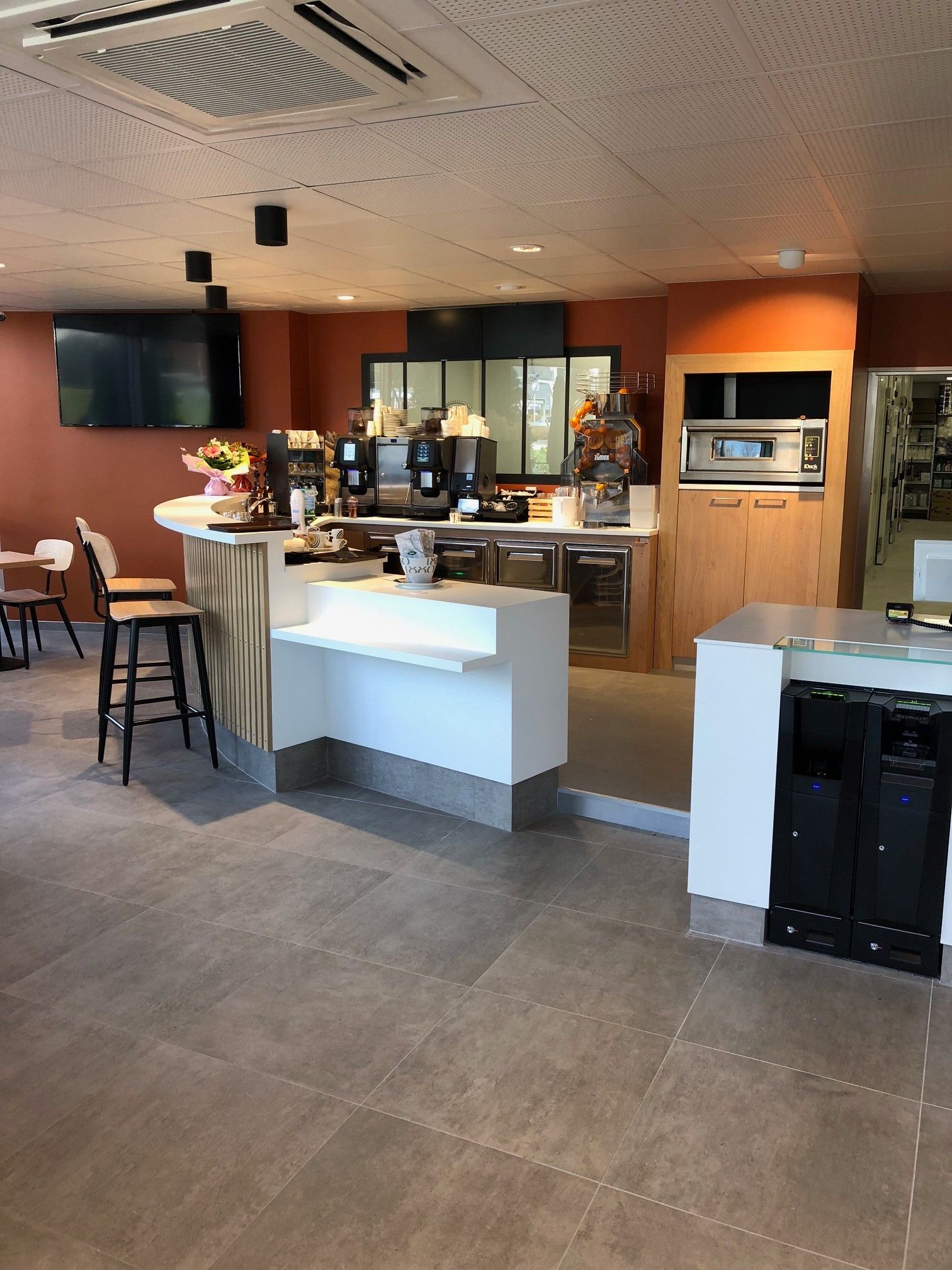 Intérieur d'un café avec bar, coin salon et espace de préparation des aliments. Dominante de couleurs orange et blanc.