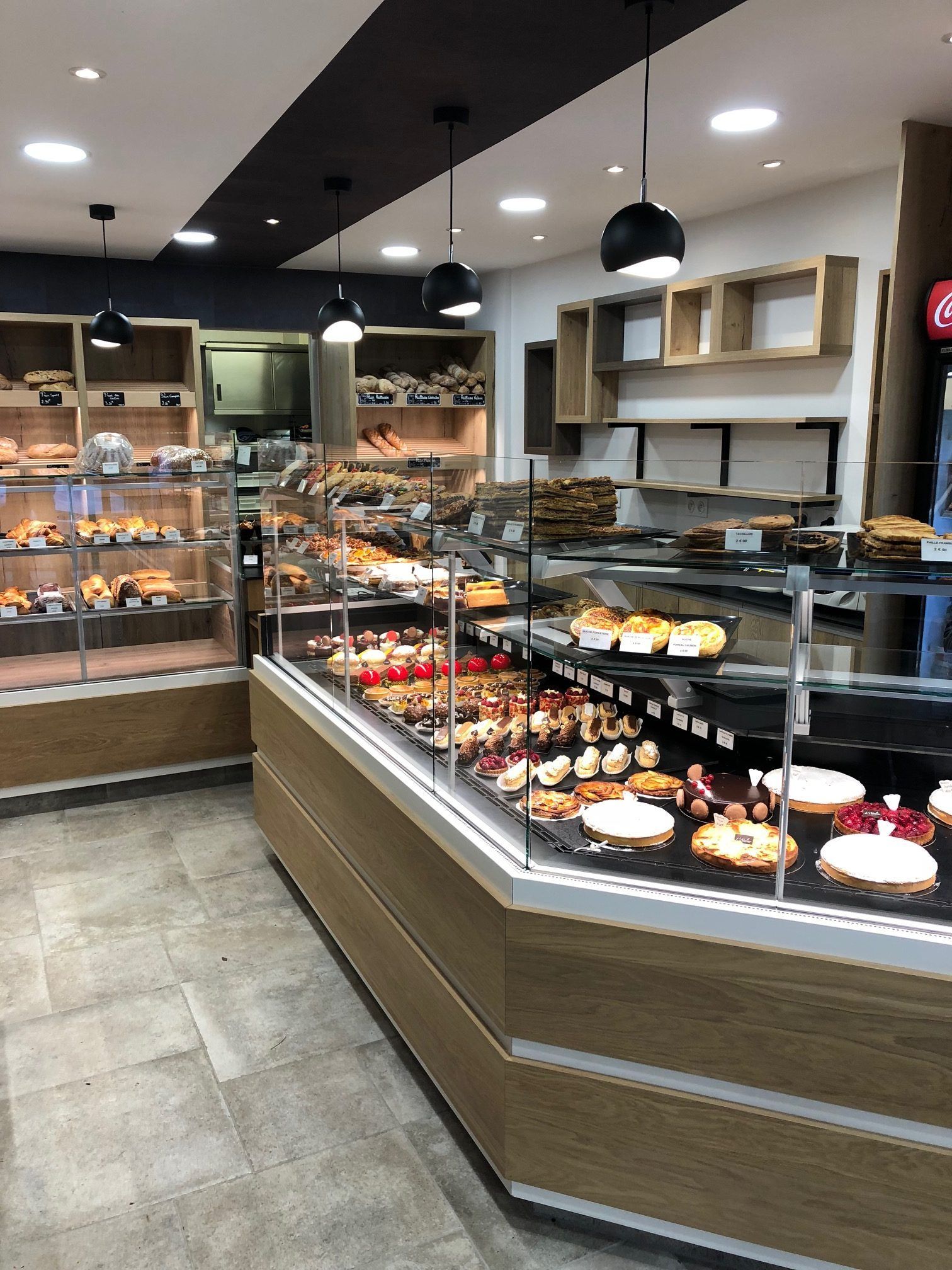 Intérieur d'une boulangerie avec vitrines remplies de viennoiseries, de pains et de desserts. Design moderne mêlant bois et verre.