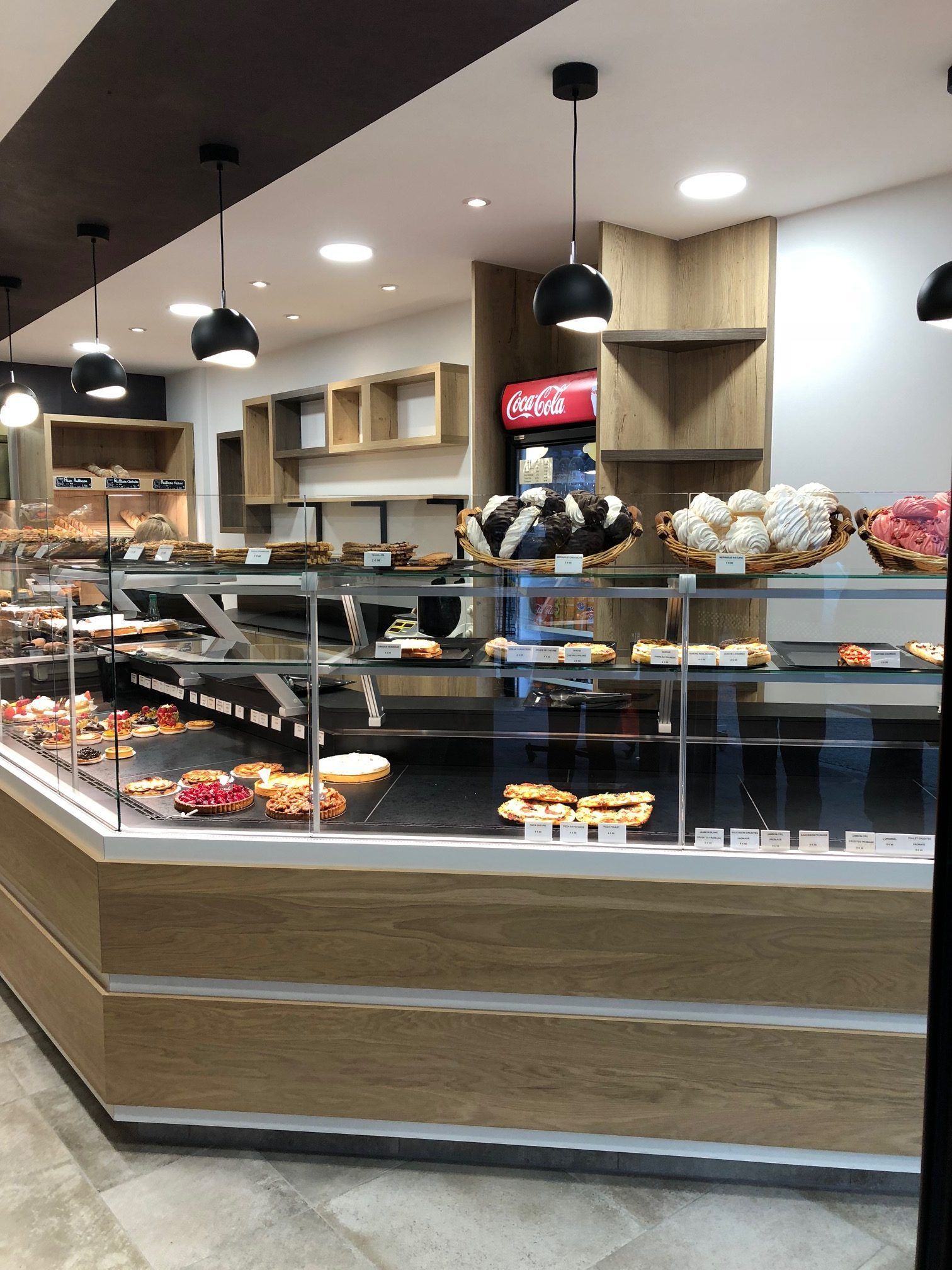 Intérieur d'une boulangerie avec vitrine à pâtisseries, étagères en bois et luminaires suspendus.