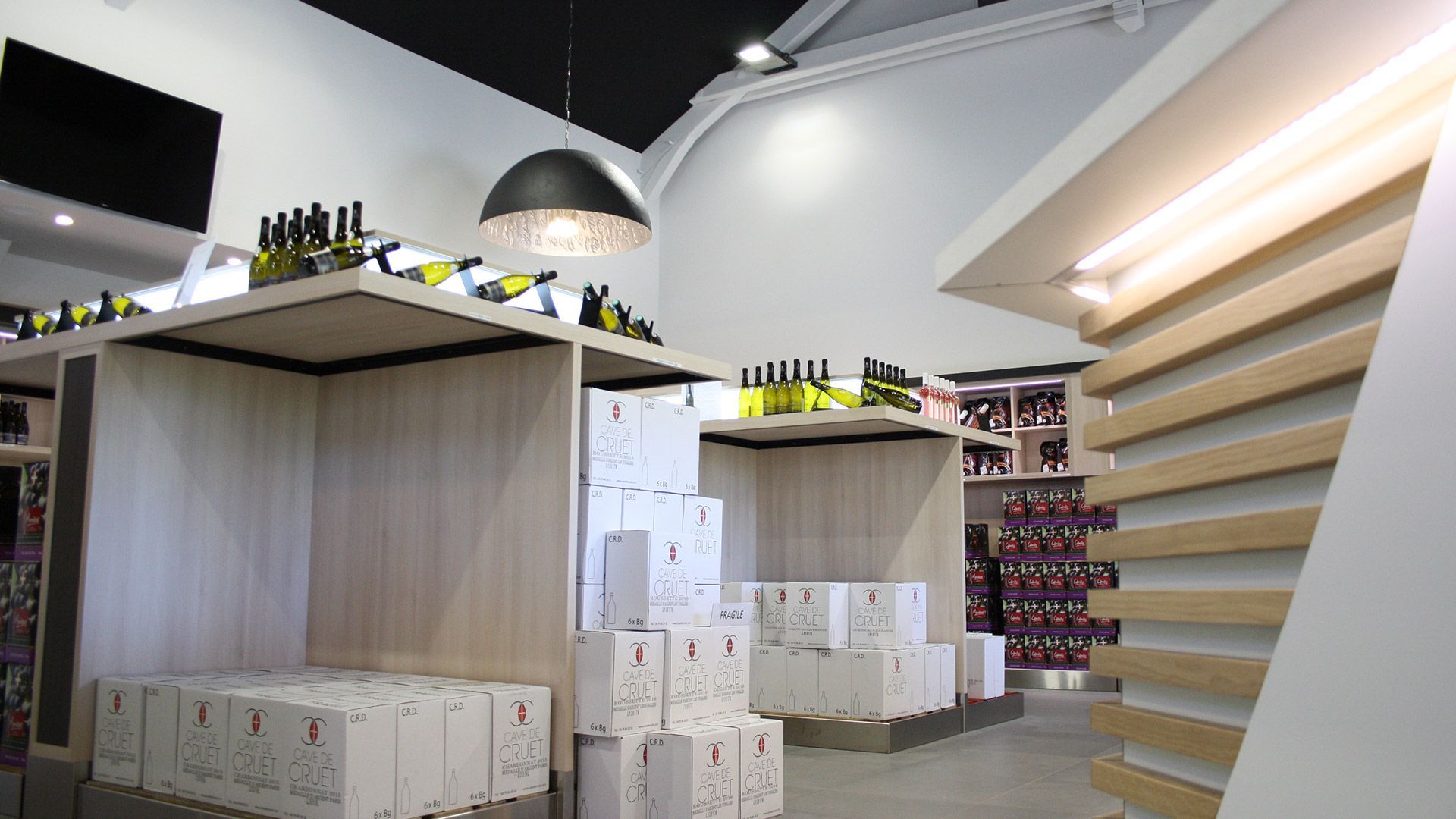 Intérieur d'une cave à vin avec des étagères en bois présentant bouteilles et caisses de vin. Palette de couleurs neutres.