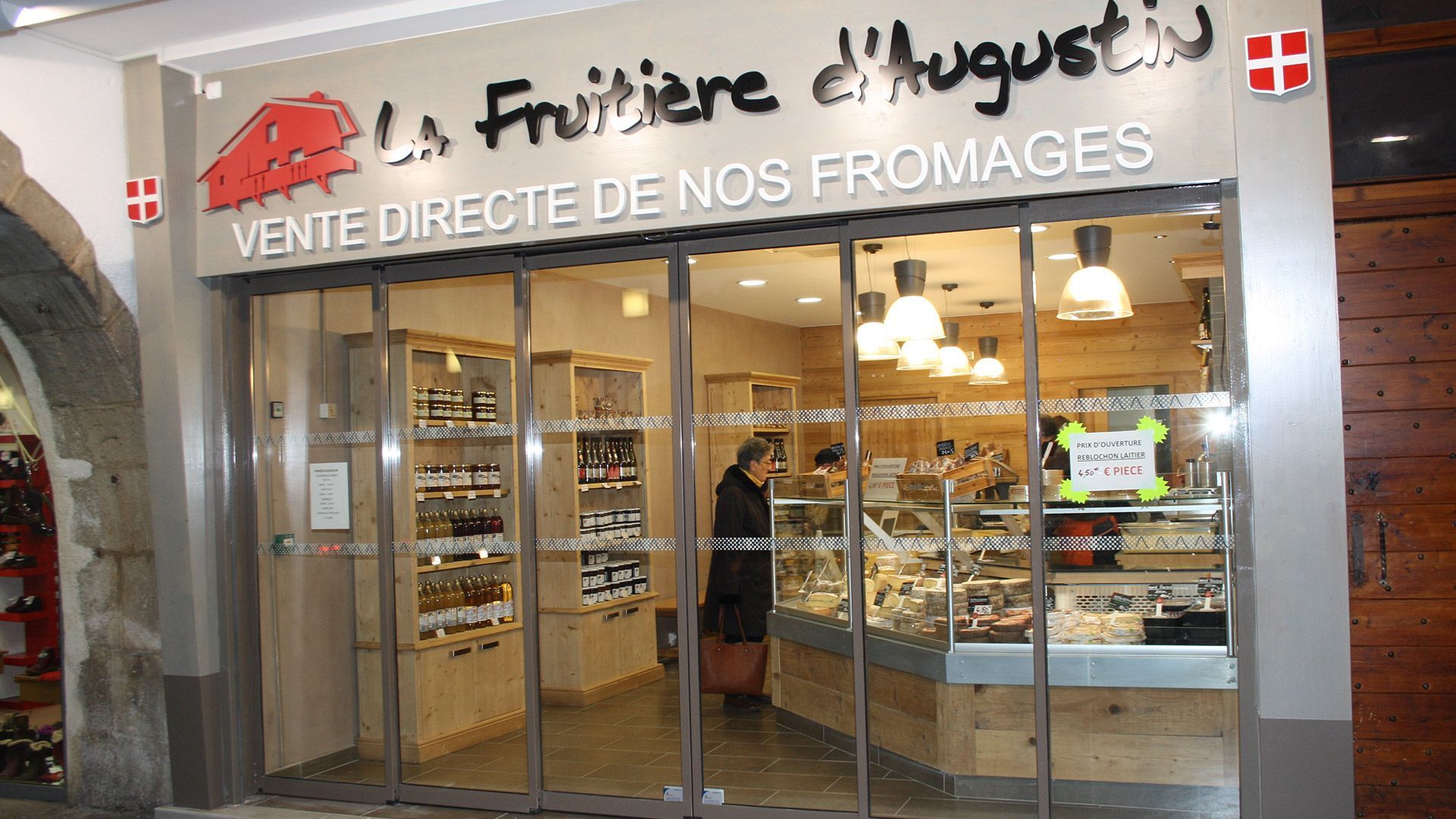 L'entrée d'une fromagerie, « La Fruitière d'Augustin » en français, avec une femme à l'intérieur.