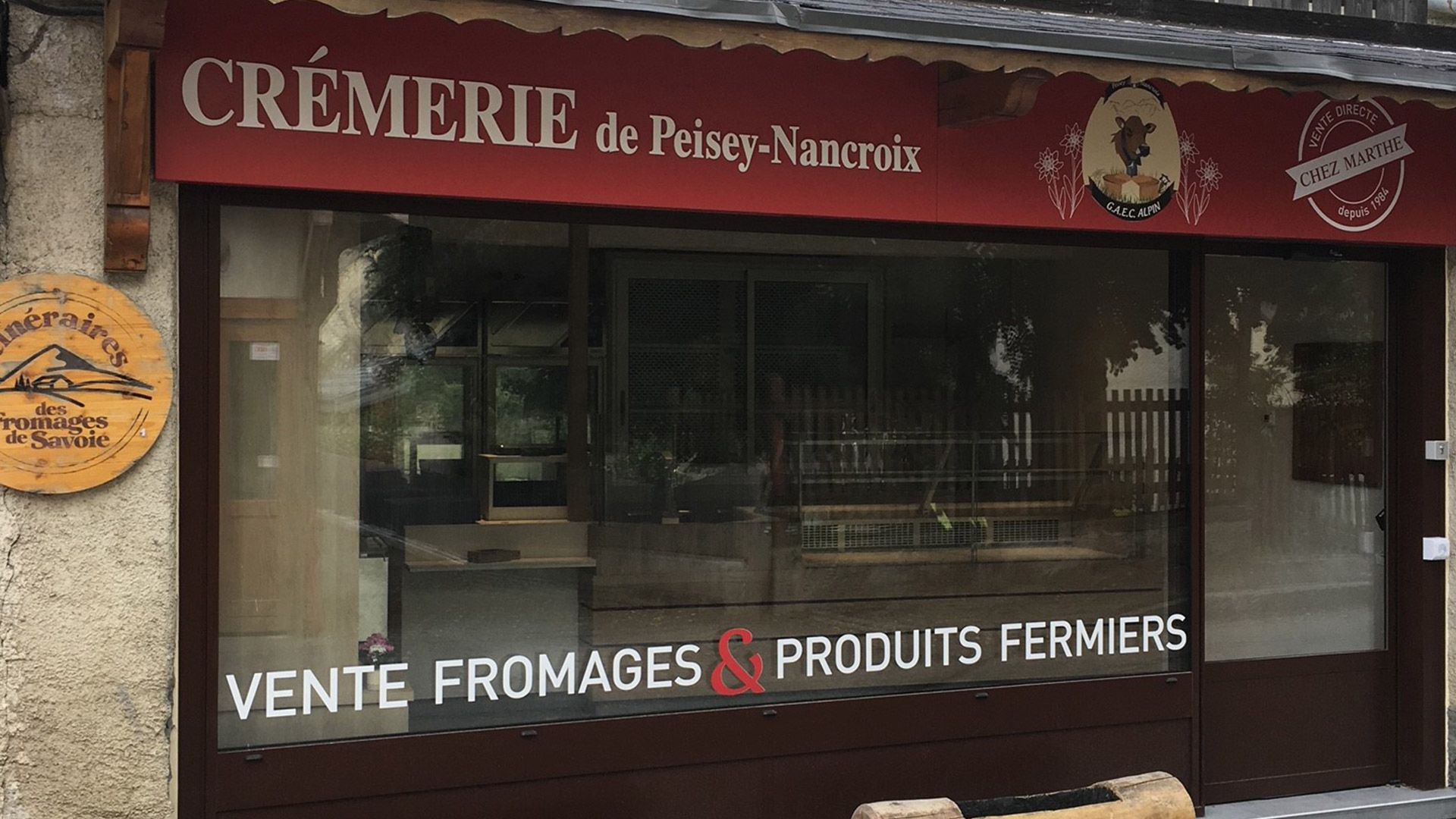 Façade de fromagerie avec auvent rouge et vitrine. L'enseigne indique « Vente de fromages et produits fermiers ».