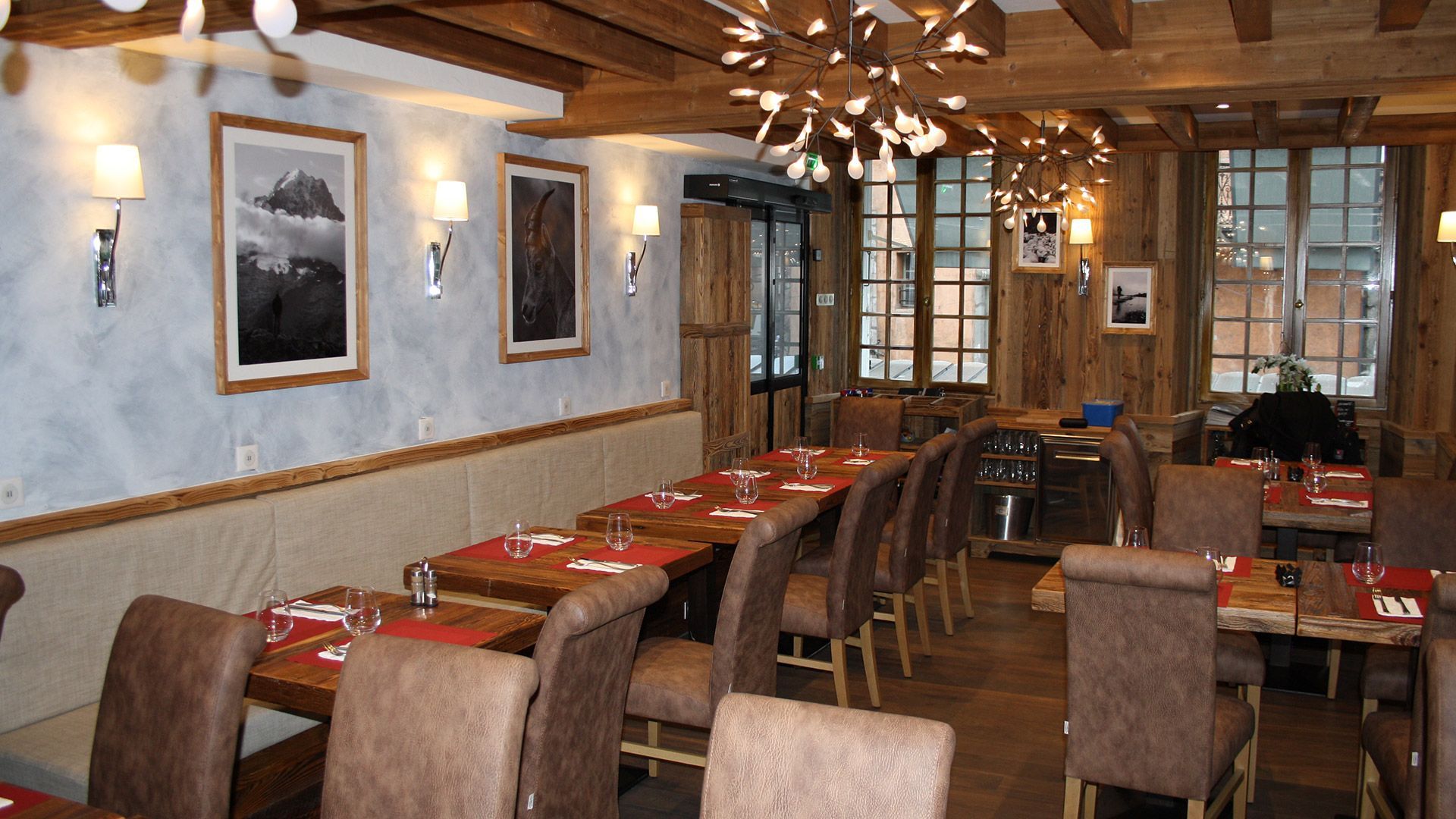 Intérieur d'un restaurant rustique avec murs en bois, tables dressées et éclairage décoratif.