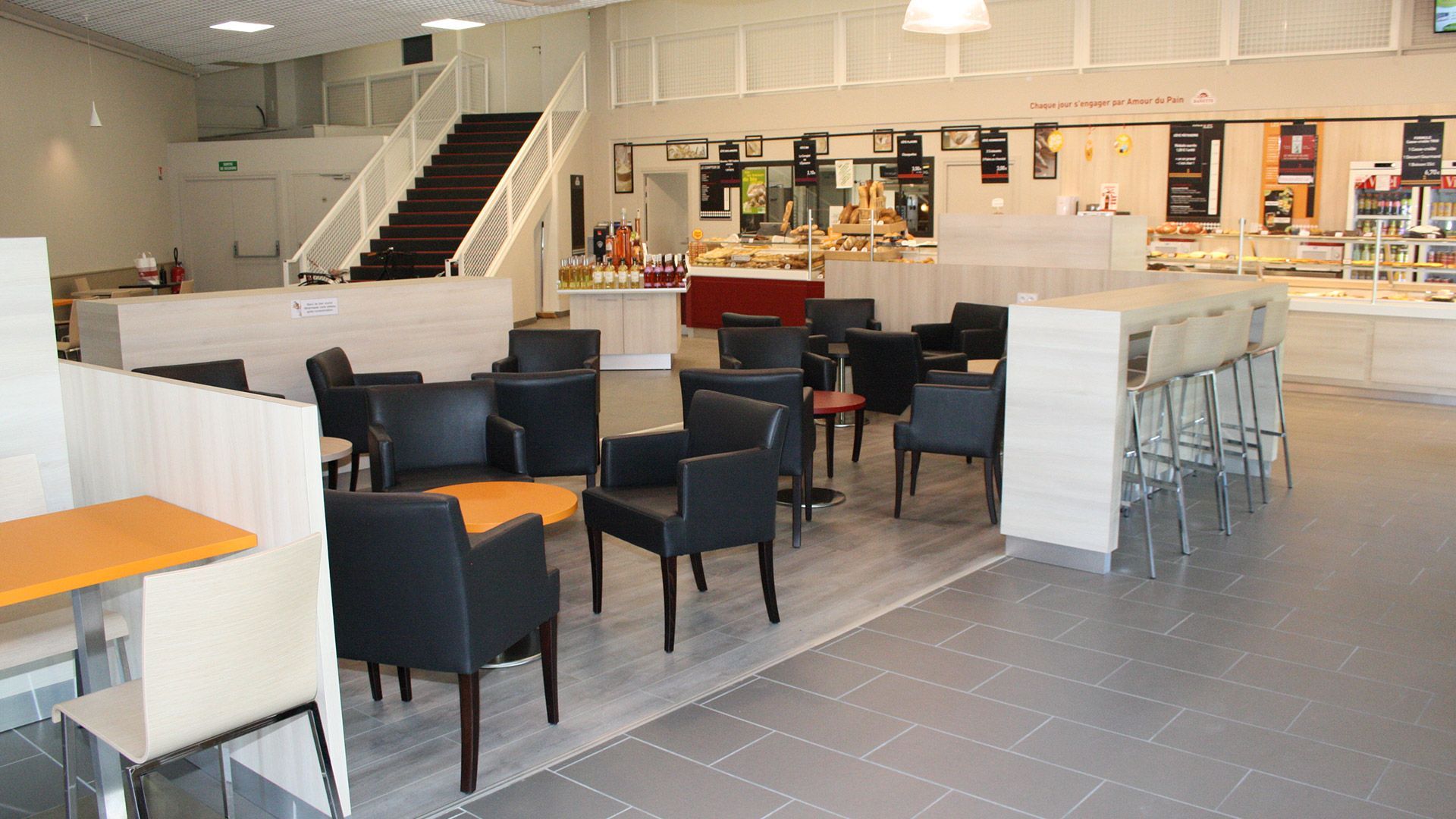 Intérieur d'un café avec tables, chaises, comptoirs de restauration et escaliers.