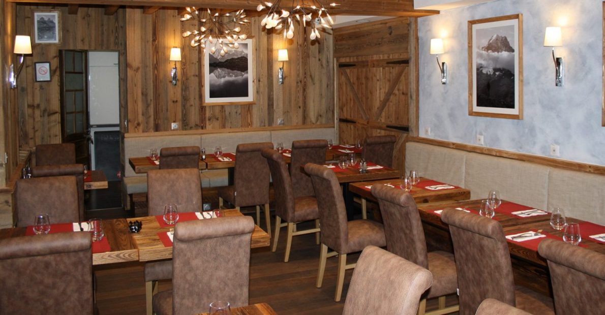 Intérieur du restaurant avec boiseries, tables et chaises, orné de tableaux et d'un éclairage chaleureux.