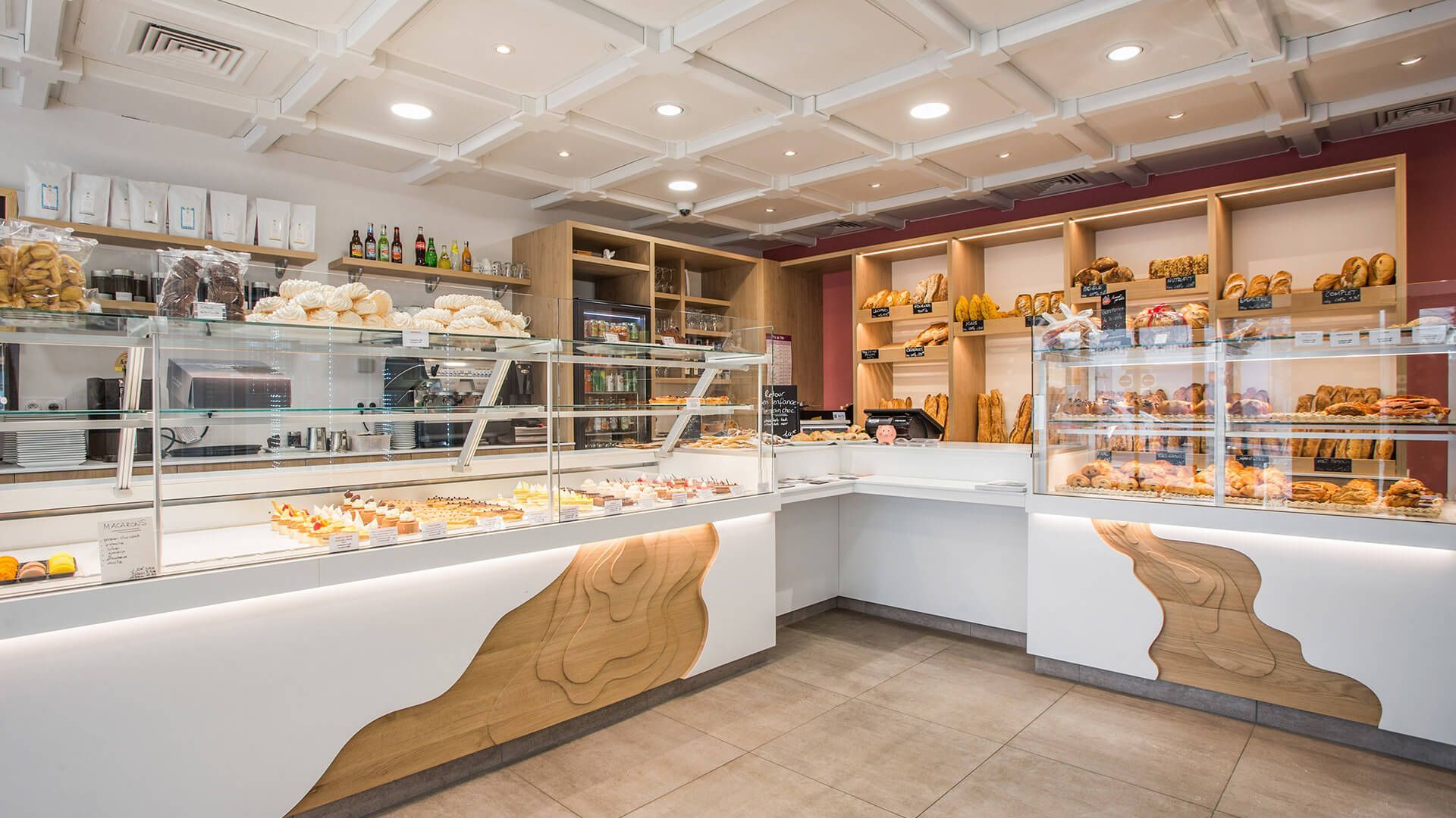 Intérieur de boulangerie avec comptoirs blancs et en bois présentant des pâtisseries et du pain ; éclairage zénithal.