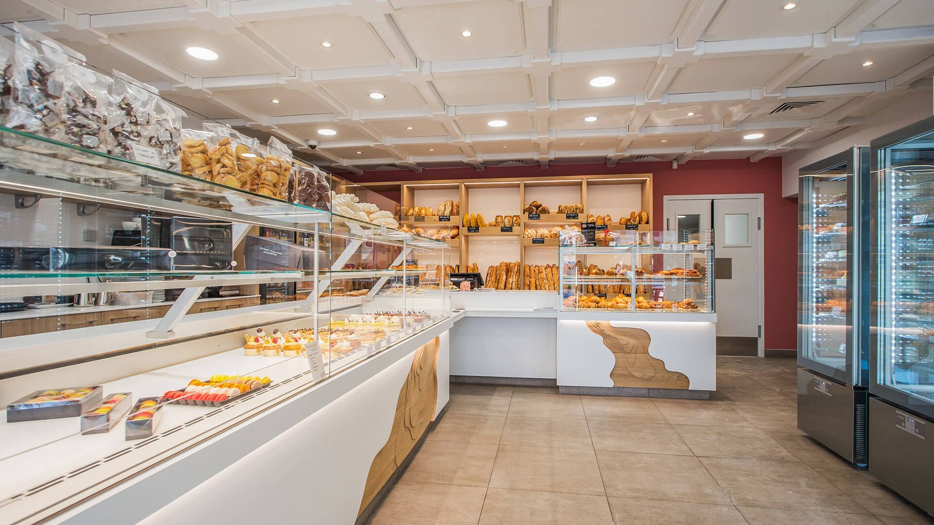 Intérieur d'une boulangerie avec des produits de boulangerie présentés dans des vitrines, des comptoirs blancs et un éclairage zénithal.