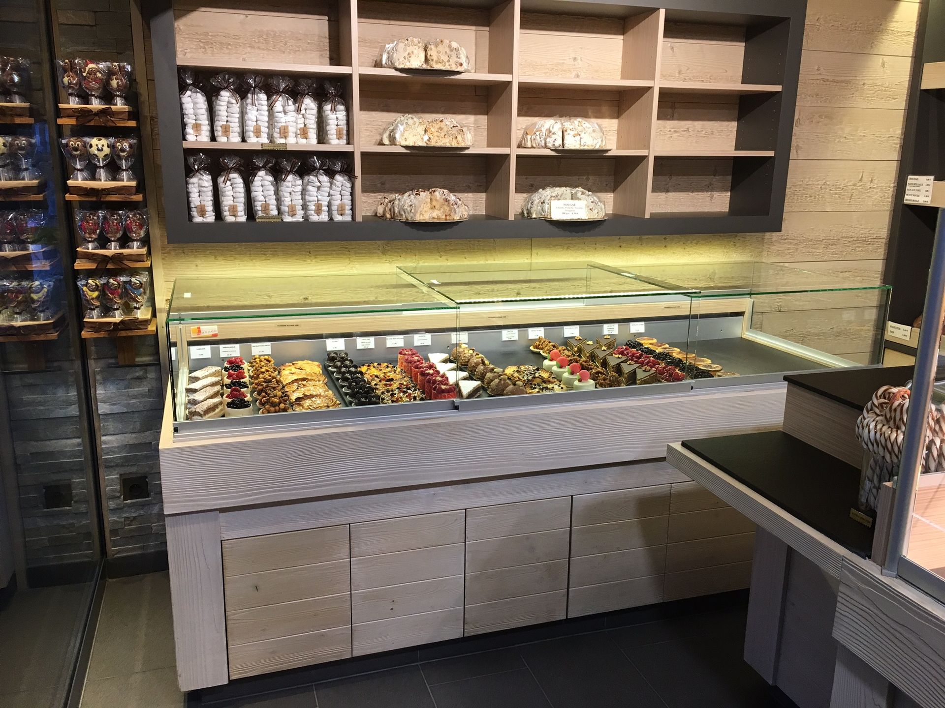 Vitrine à pâtisseries dans une boulangerie, présentant divers desserts. Les étagères supérieures contiennent des bocaux et d'autres produits de boulangerie.