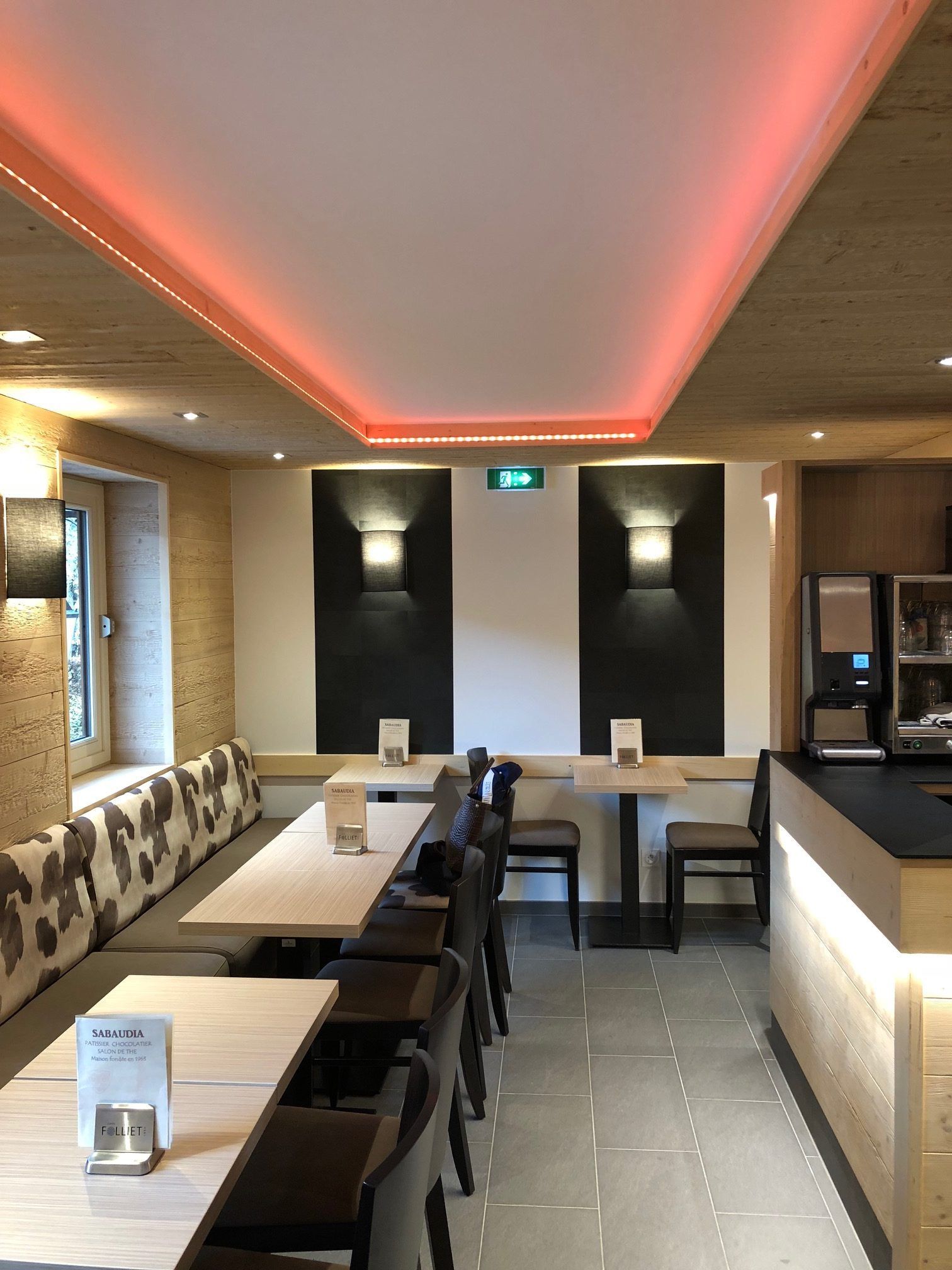 Intérieur du restaurant avec tables, chaises et banquettes, mis en valeur par un éclairage rouge et des boiseries.