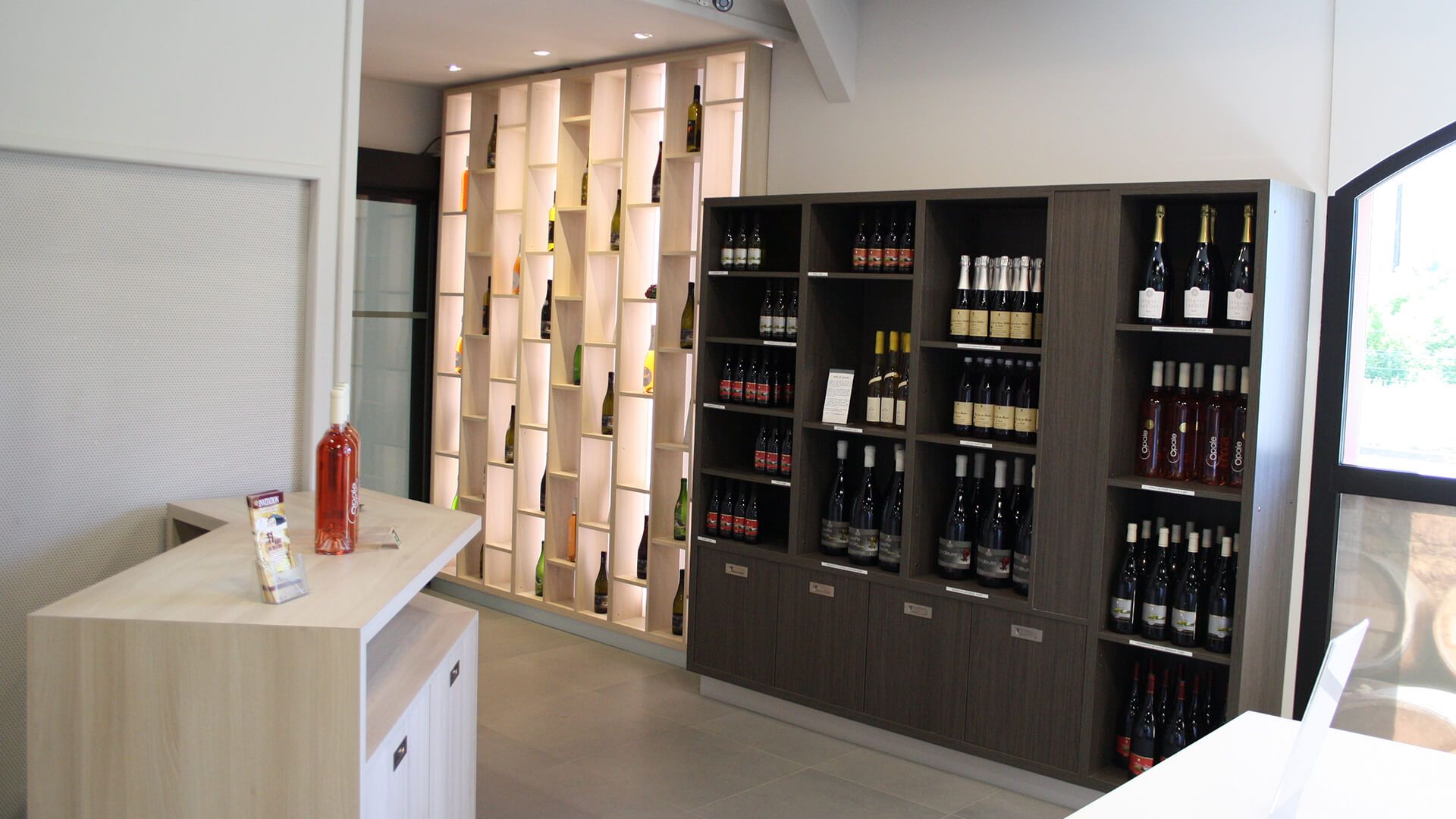 Intérieur d'une cave à vin avec des étagères en bois présentant des bouteilles de vin. Cloison en bois clair en arrière-plan.