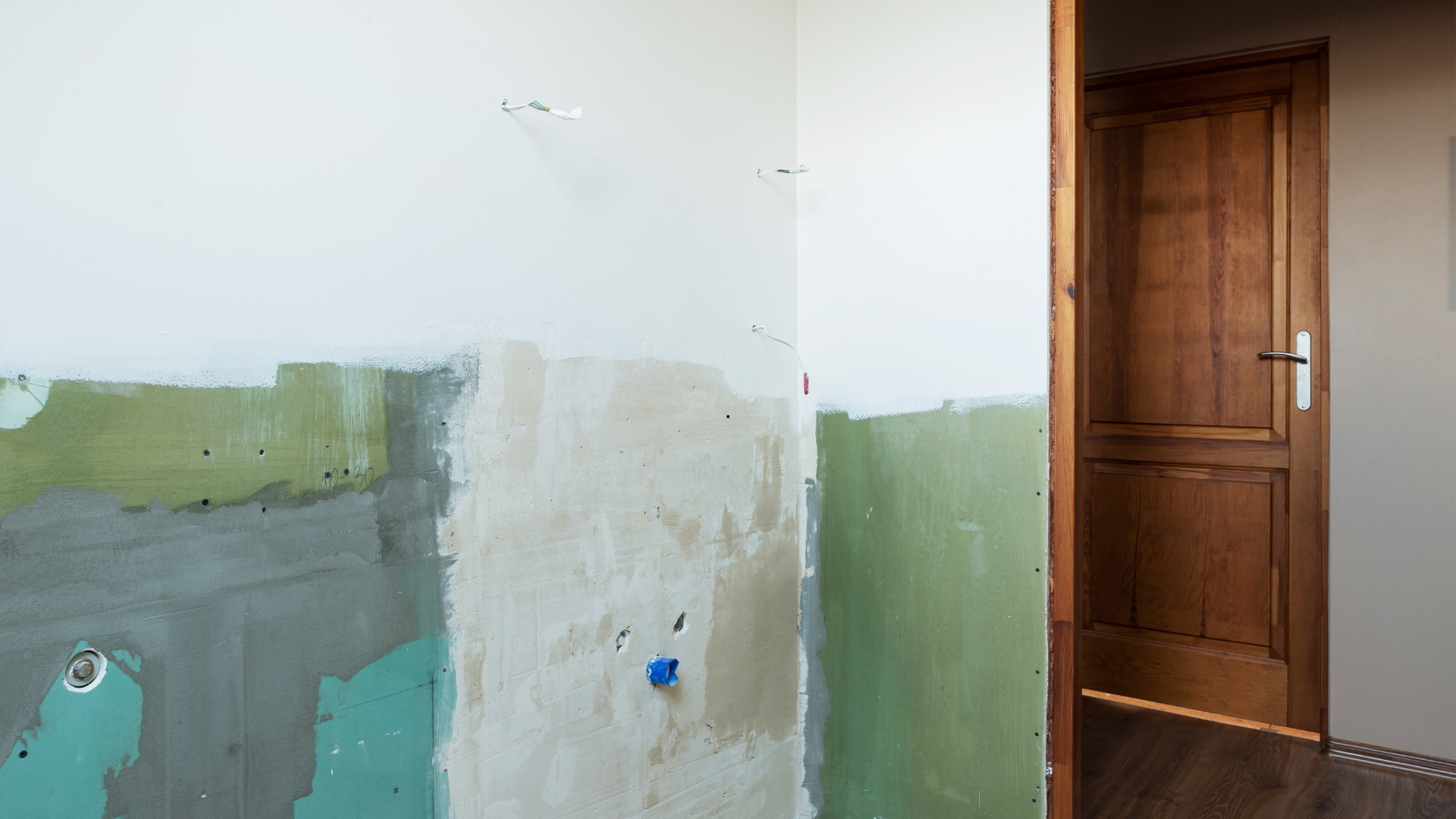 Mur en construction avec couches de peinture apparentes et une porte.