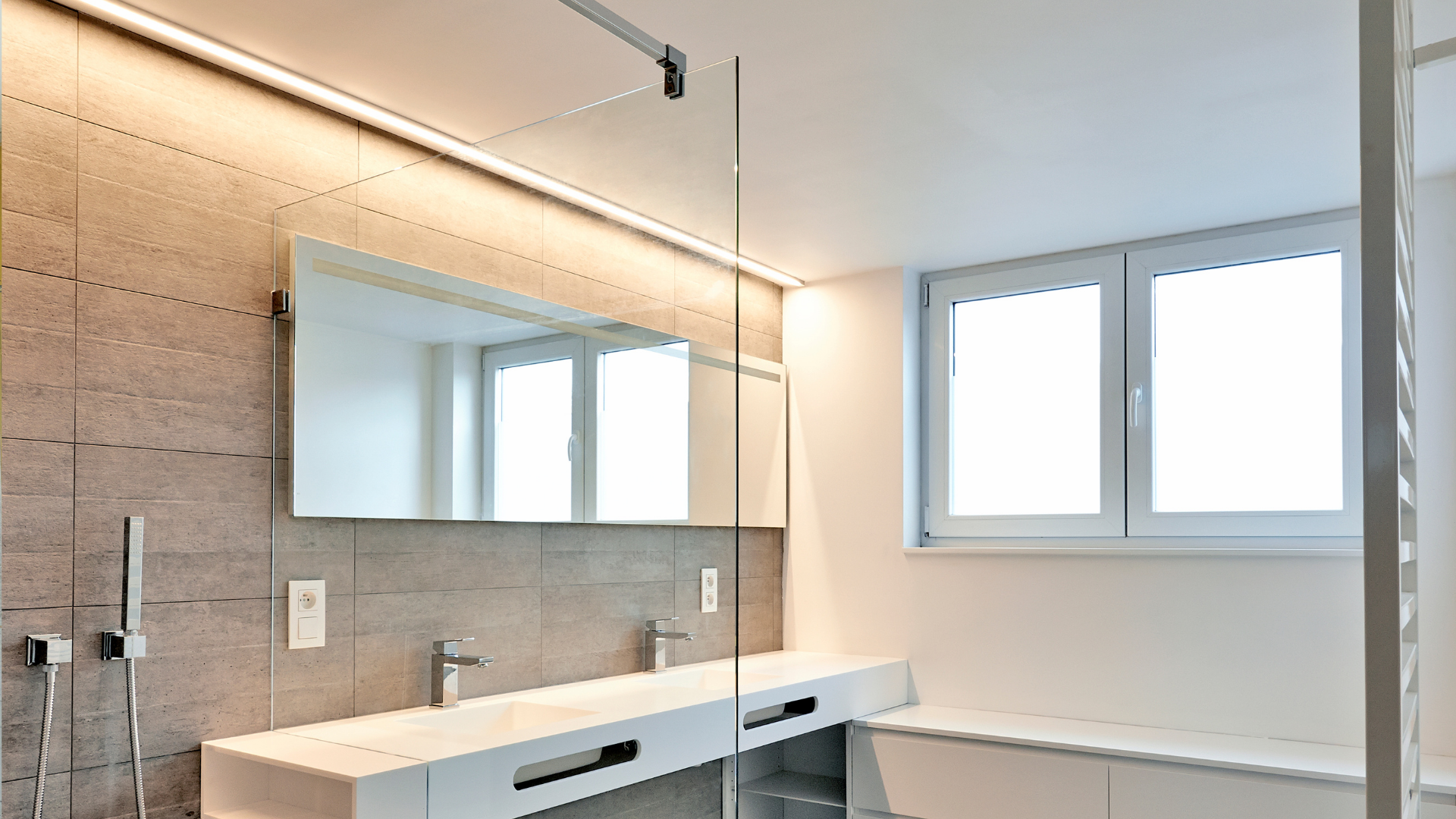 Salle de bain moderne avec un grand miroir, des comptoirs blancs et une fenêtre.