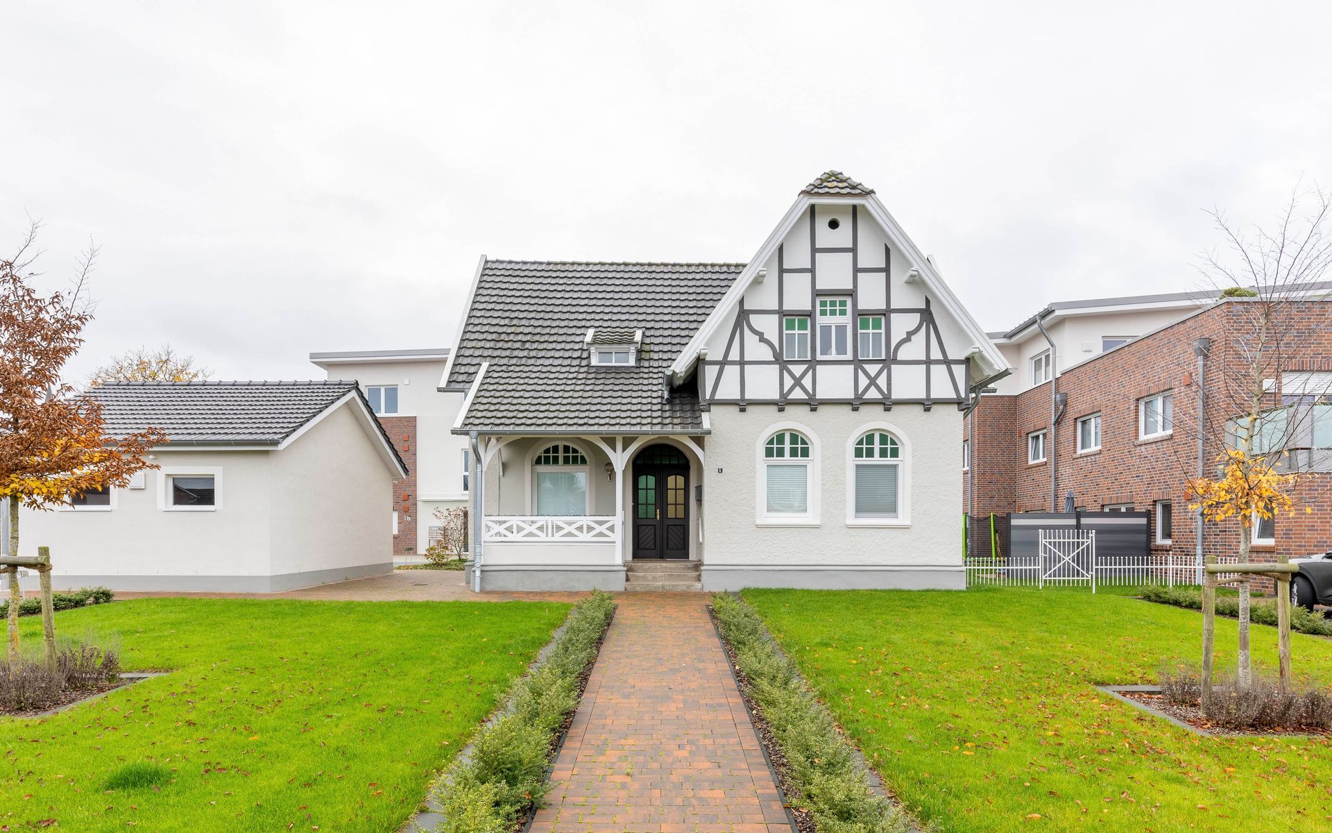 Ein weißes Haus mit einem Backsteingebäude im Hintergrund und einem Gehweg, der dorthin führt.