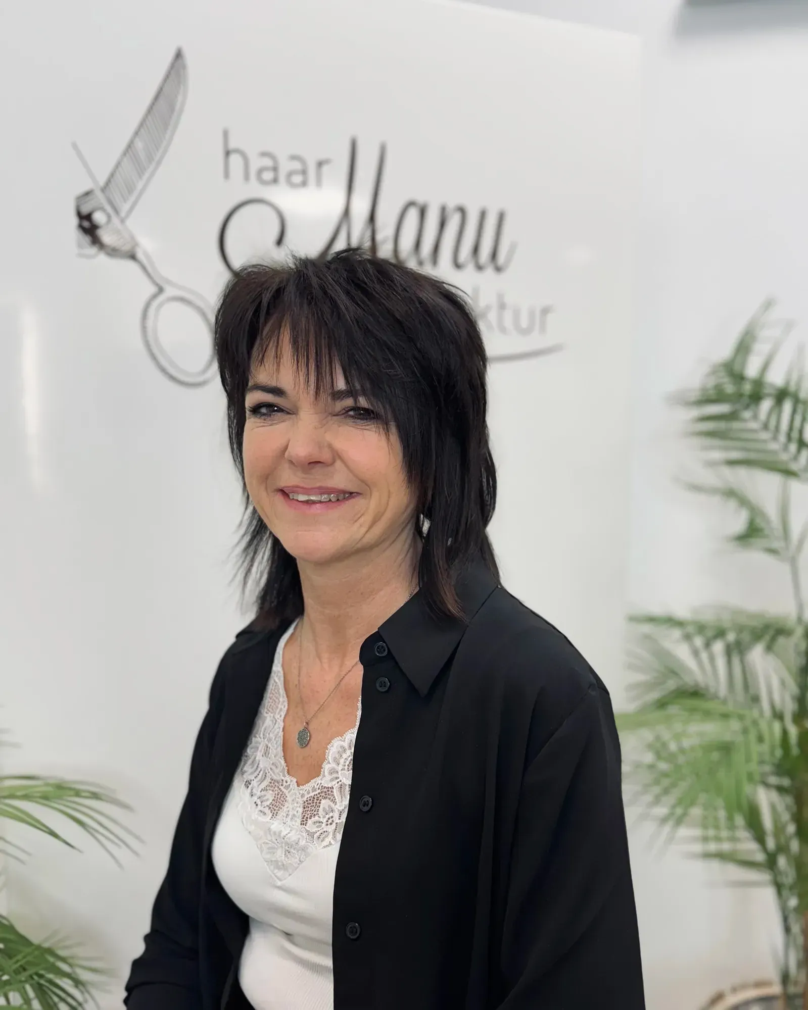 Eine Frau steht vor einem Schild mit der Aufschrift „Haar Manu“