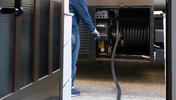 Une personne en jean et veste bleue actionne un équipement à l'aide d'un tuyau d'arrosage sur un camion.