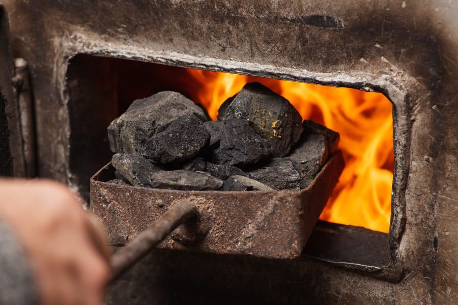 Une poignée de charbon dans une pelle métallique pénètre dans un four aux flammes d'un orange vif.