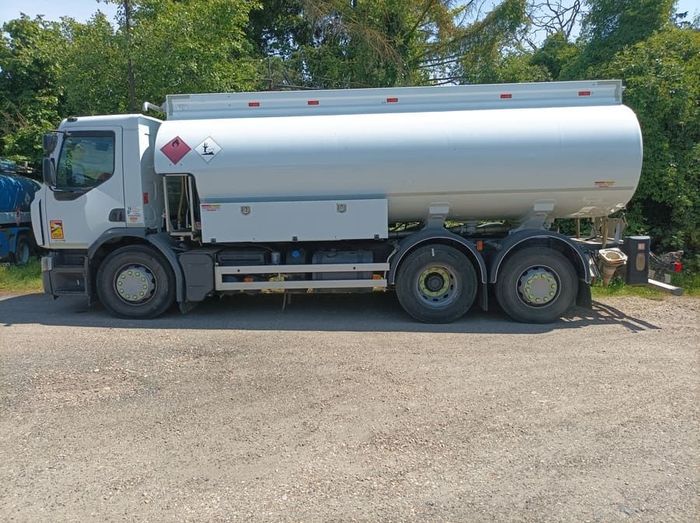 Camion-citerne blanc stationné sur du gravier, avec des arbres en arrière-plan.