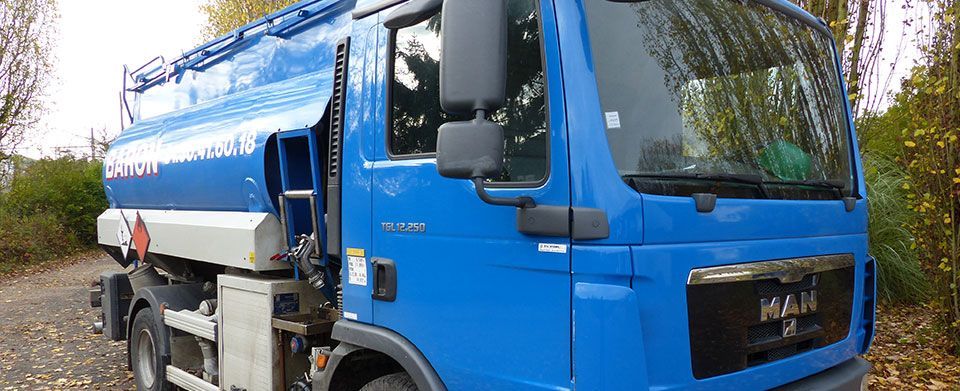 Camion-citerne bleu stationné sur un chemin de gravier, avec de la végétation en arrière-plan.
