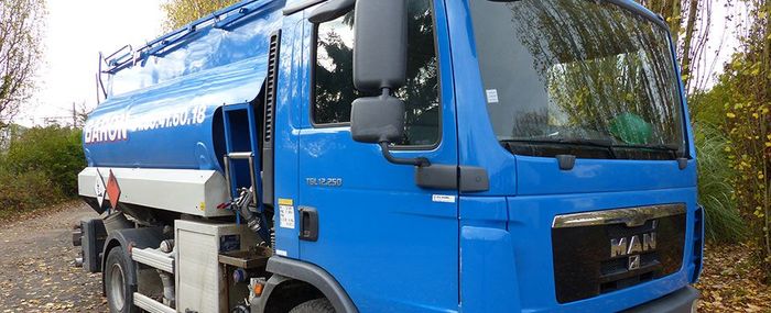 Camion-citerne bleu stationné sur un chemin de gravier, avec de la végétation en arrière-plan.