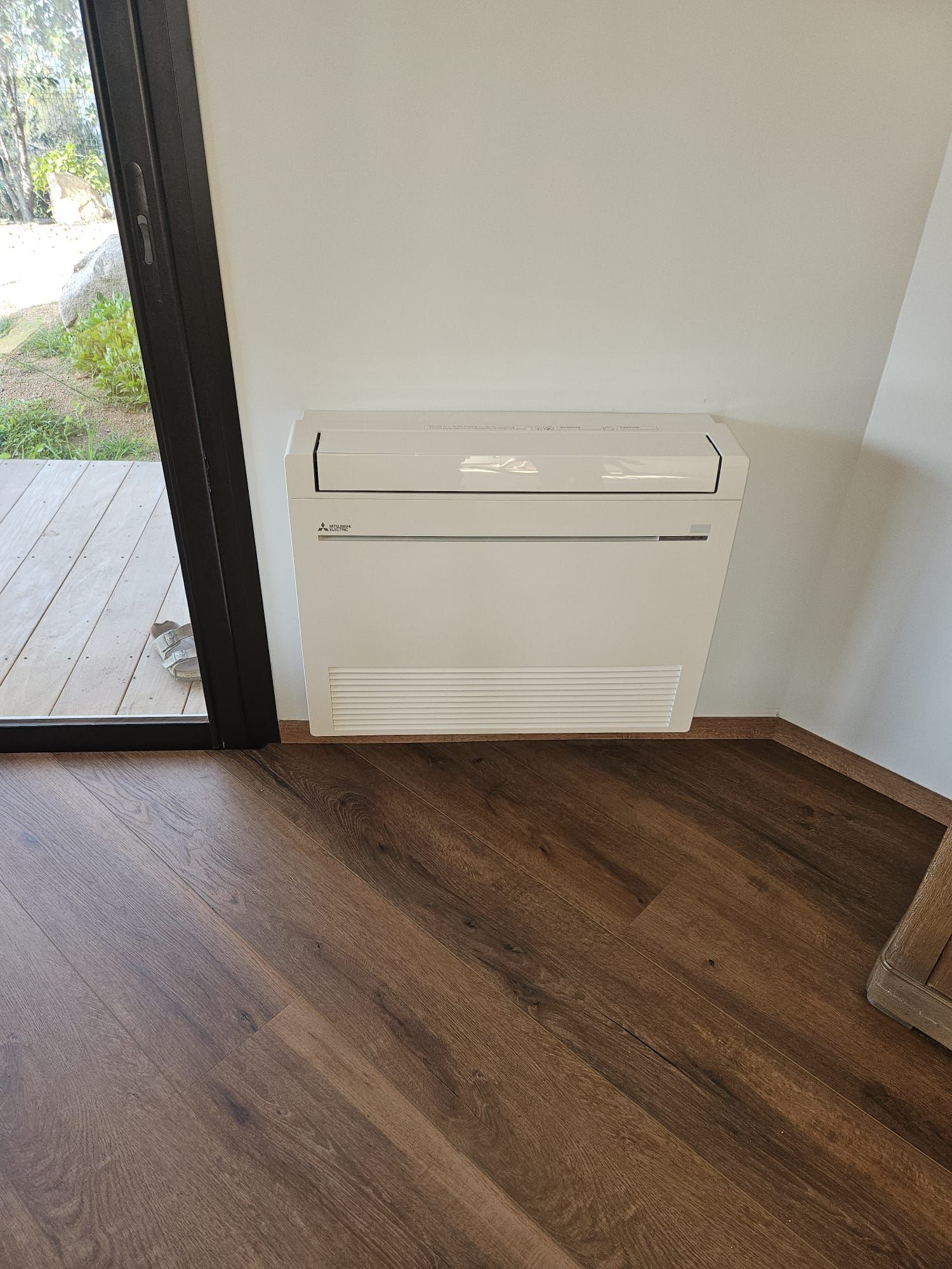 Chauffage mural blanc à côté d'une porte vitrée sur un sol en bois.