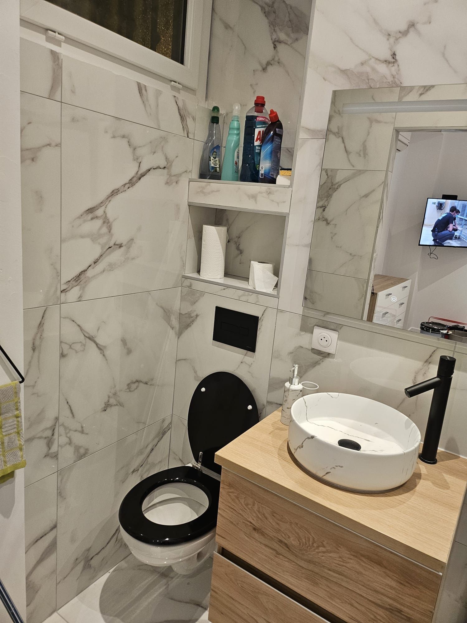 Salle de bains moderne avec carrelage en marbre, toilettes ouvertes, meuble lavabo en bois, lavabo rond et niche murale avec articles de toilette.