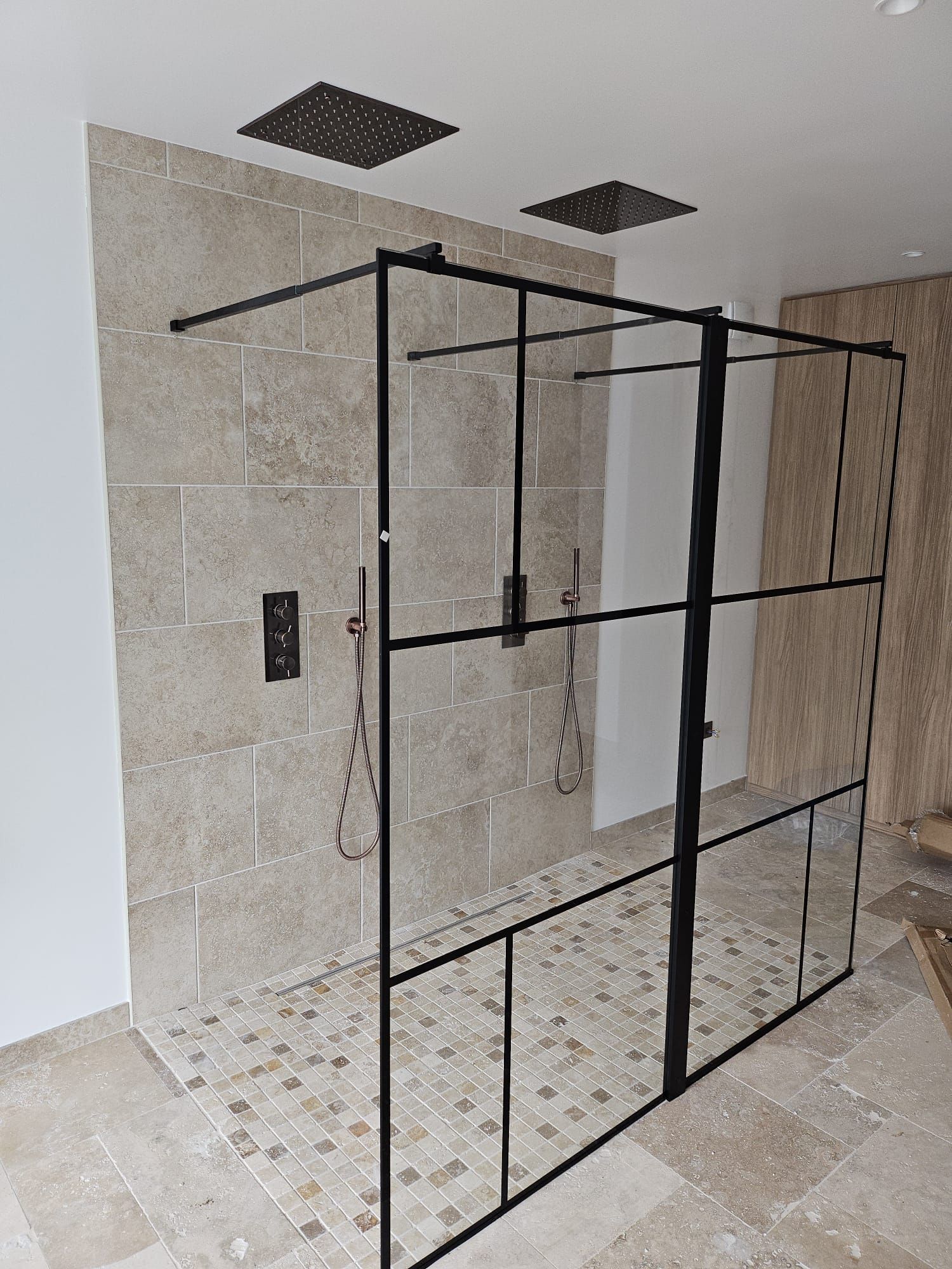 Cabine de douche en métal noir dans une salle de bains carrelée aux murs et au plafond blancs.
