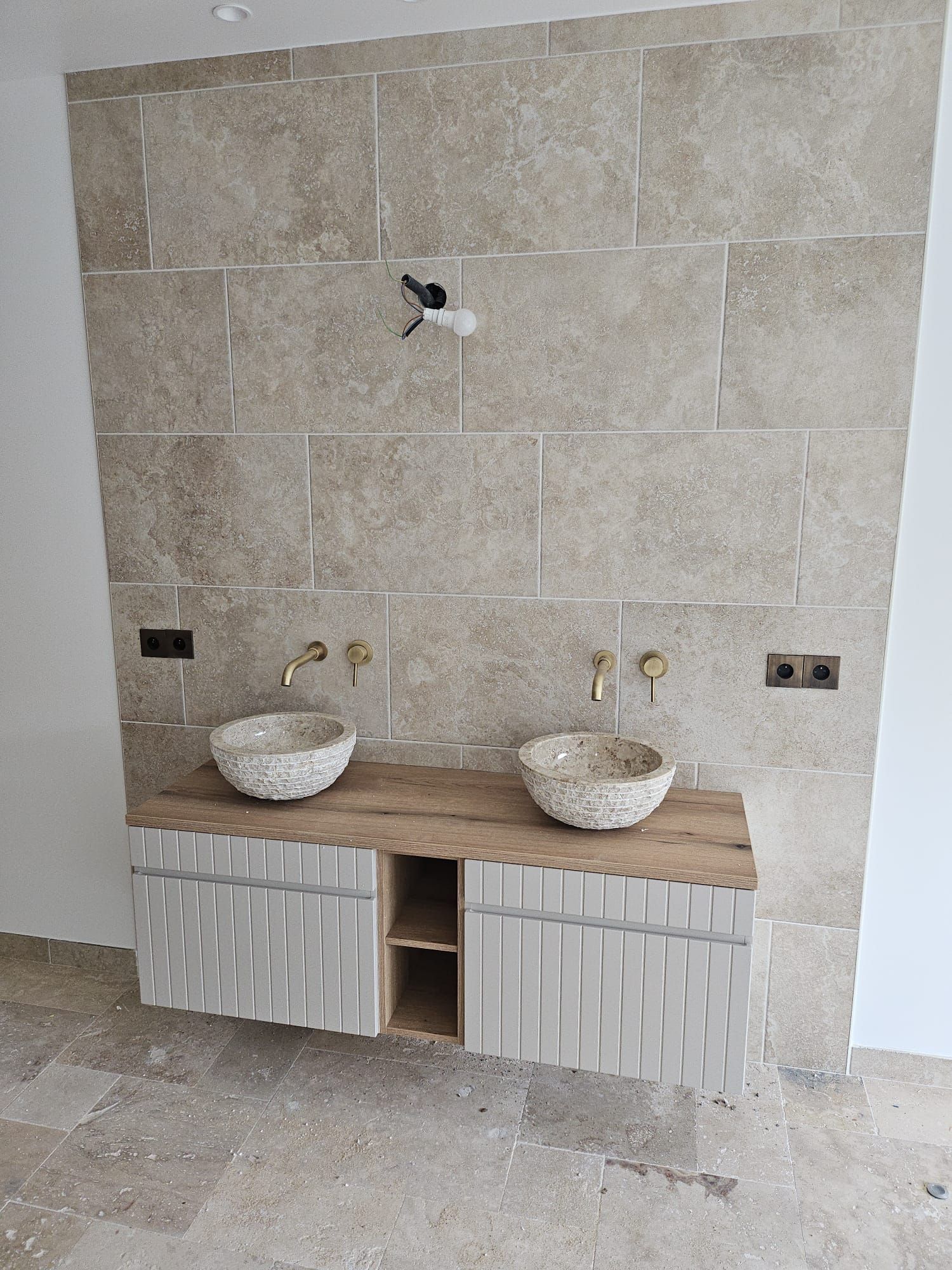 Meuble lavabo moderne en cours de réalisation, comprenant deux vasques, un comptoir en pierre et un mur carrelé.
