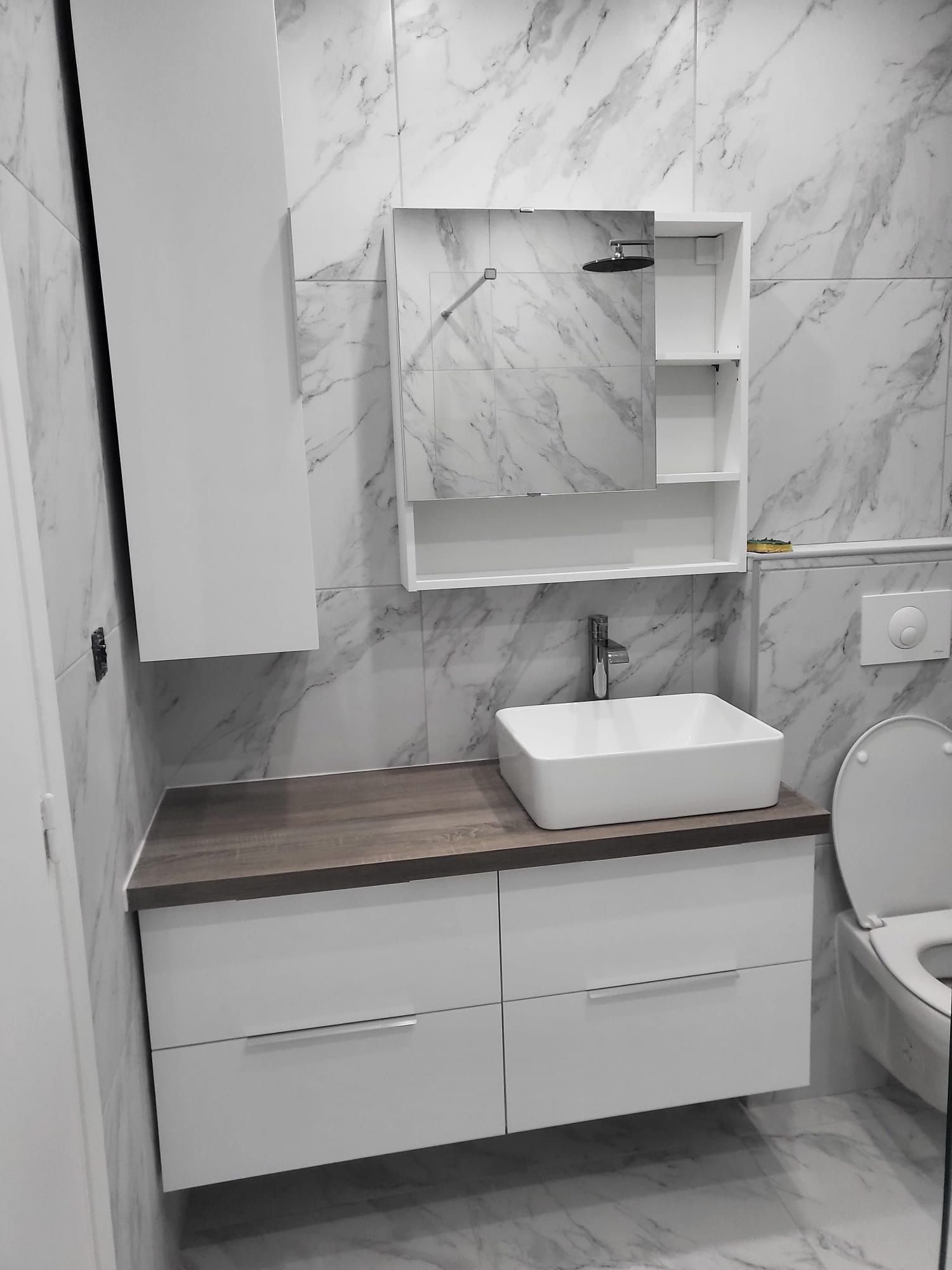 Meuble-lavabo avec comptoir en bois, lavabo blanc, armoire à miroir et toilettes à droite.