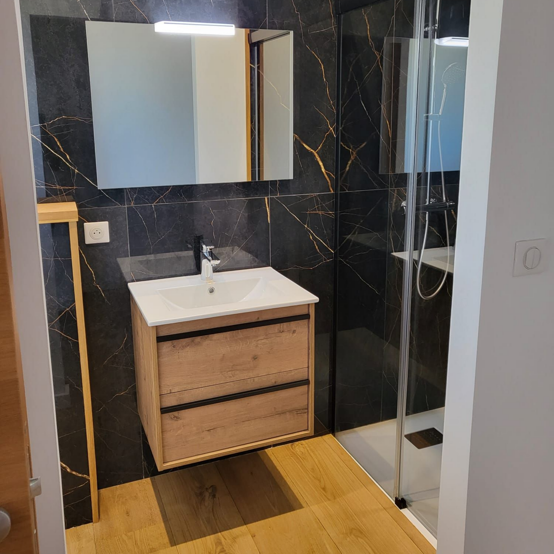 Salle de bains moderne avec murs en marbre noir, meuble lavabo en bois, miroir et cabine de douche en verre