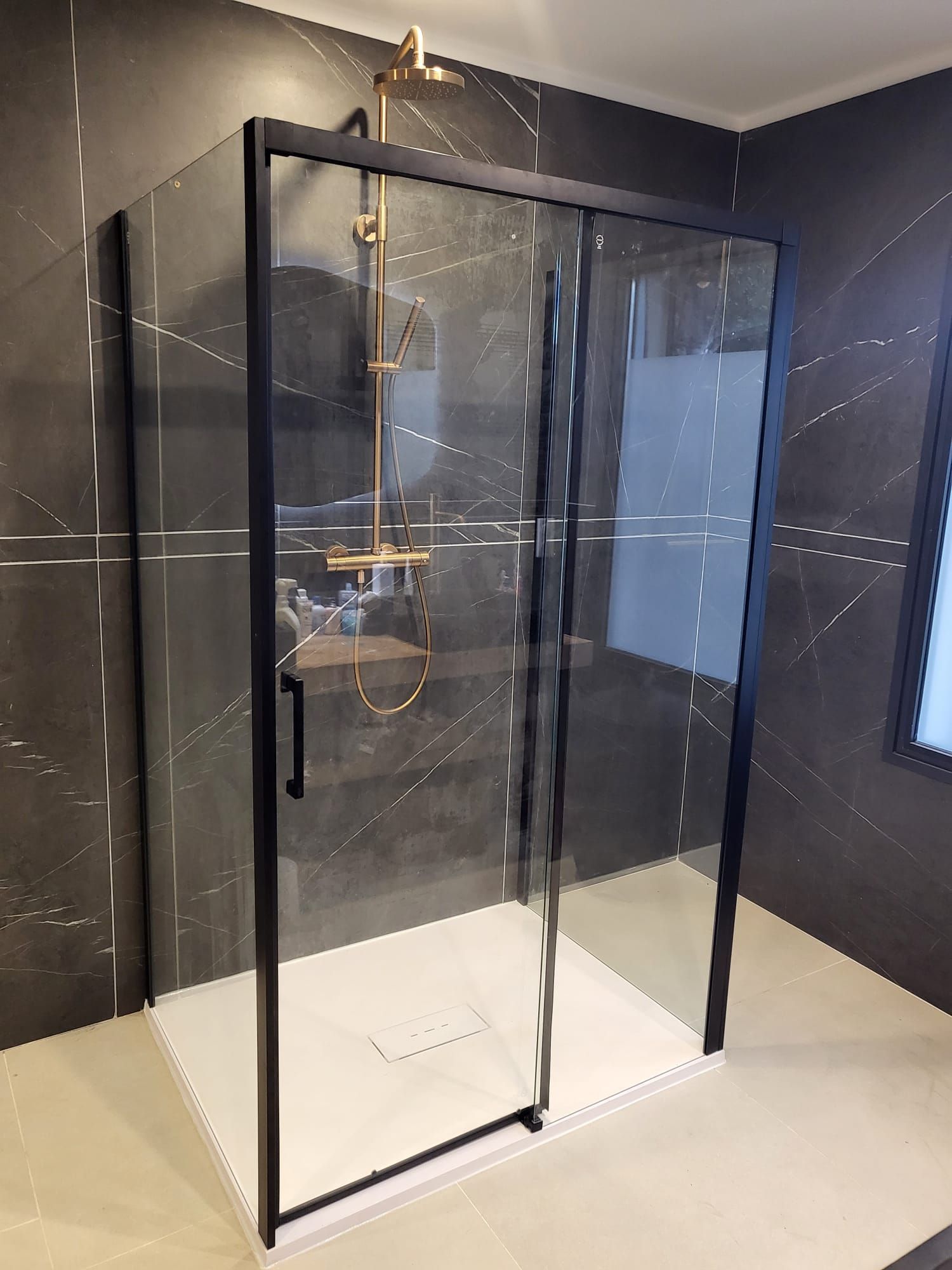 Douche à l'italienne moderne avec portes en verre noir et murs carrelés foncés dans une salle de bains lumineuse.