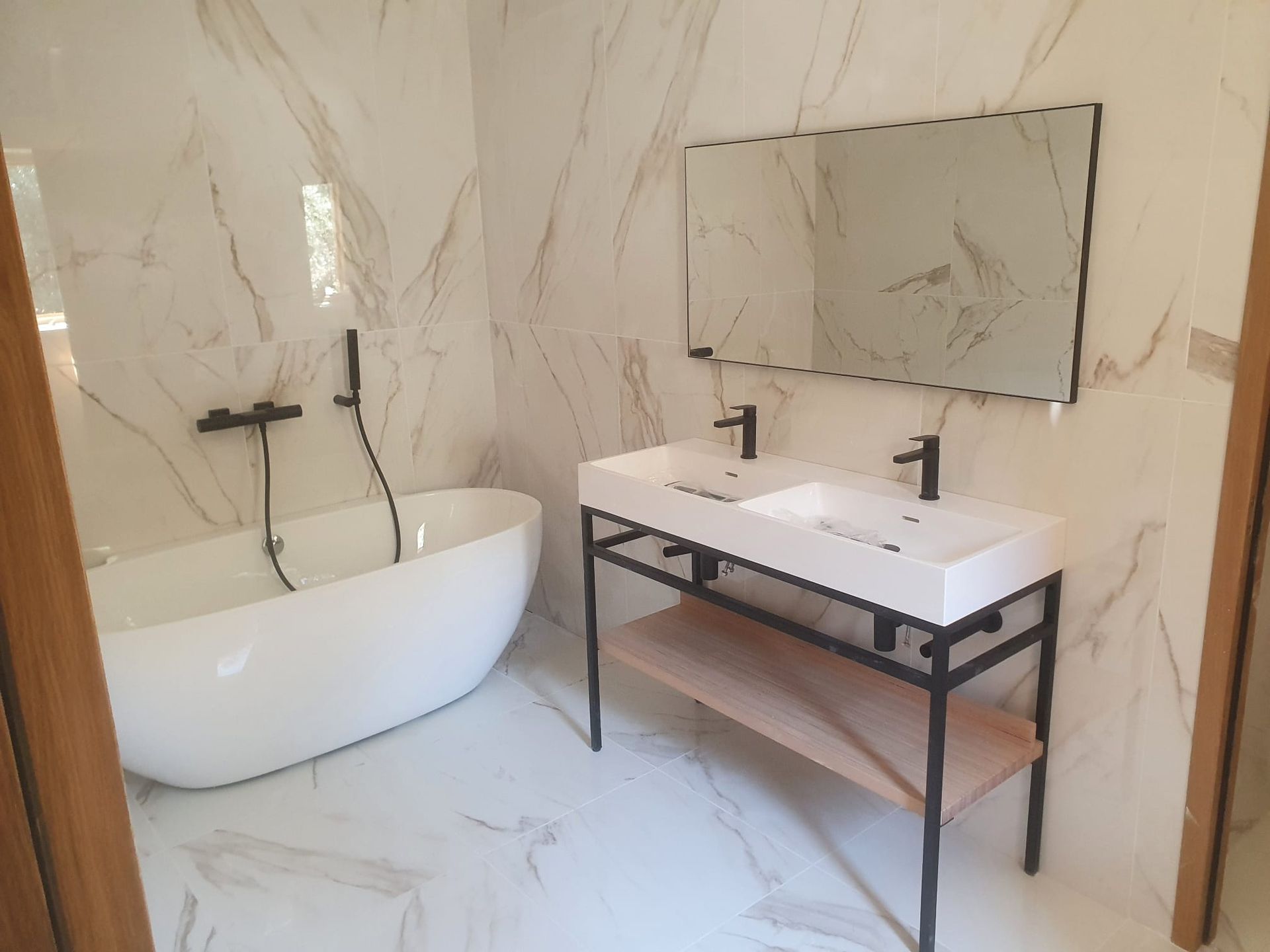 Salle de bains moderne avec baignoire îlot, meuble-lavabo et grand miroir sur murs imitation marbre.