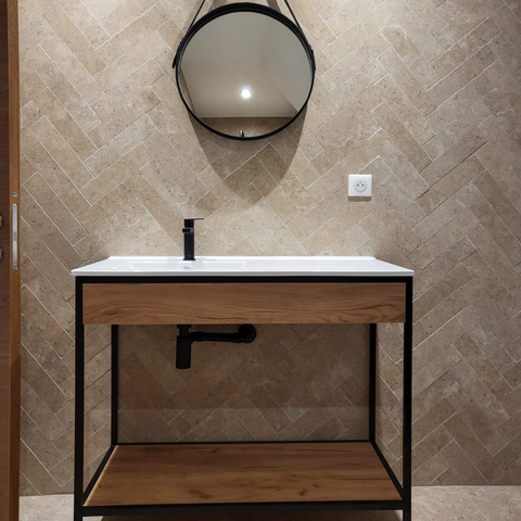 Meuble lavabo moderne avec miroir rond, robinet noir et mur carrelé beige.