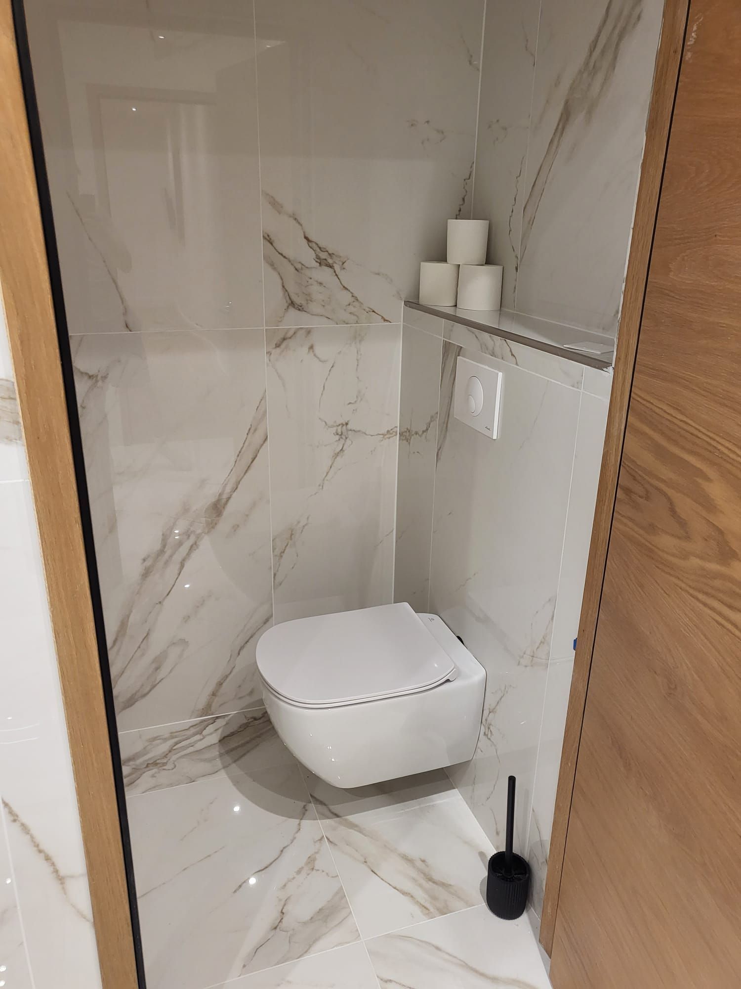 Petite salle de bains moderne avec toilettes suspendues, carrelage en marbre et porte en bois.