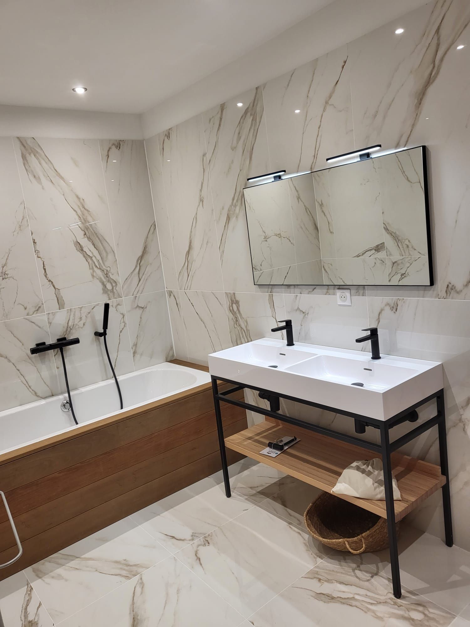 Salle de bains moderne avec murs imitation marbre, baignoire, douche murale, meuble lavabo et miroir.