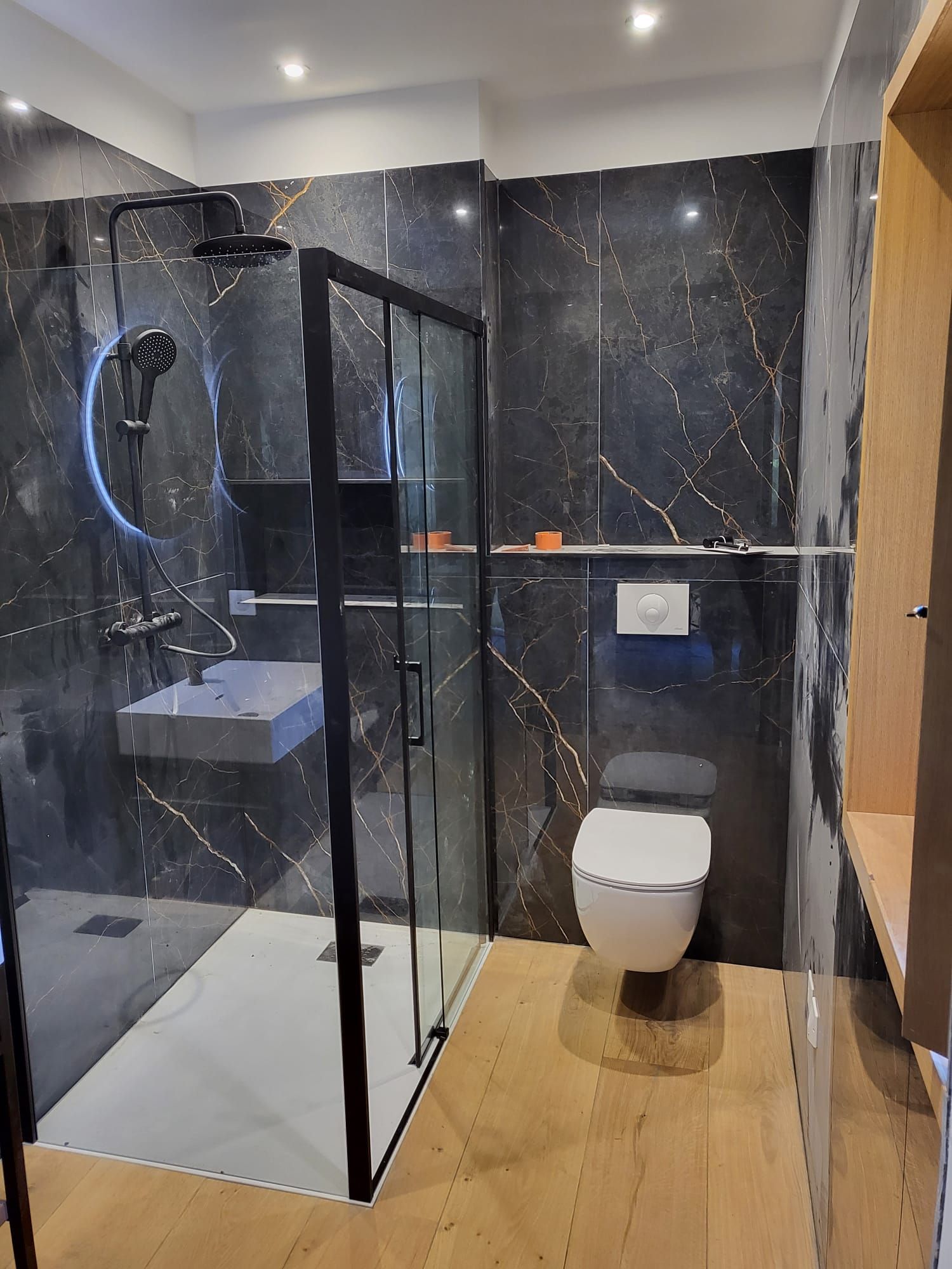 Salle de bains moderne avec cabine de douche en marbre noir, WC suspendu et parquet clair
